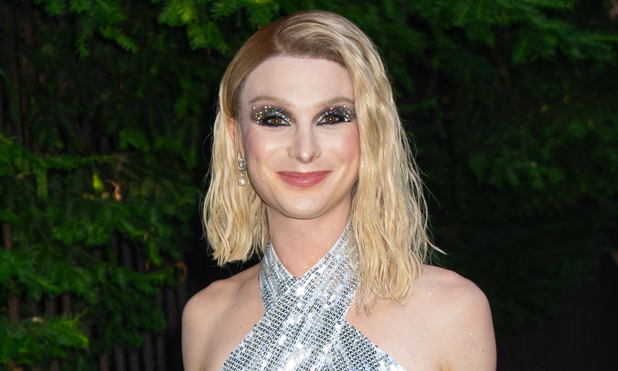 Dylan Mulvaney, in a silver dress, walking down a street.