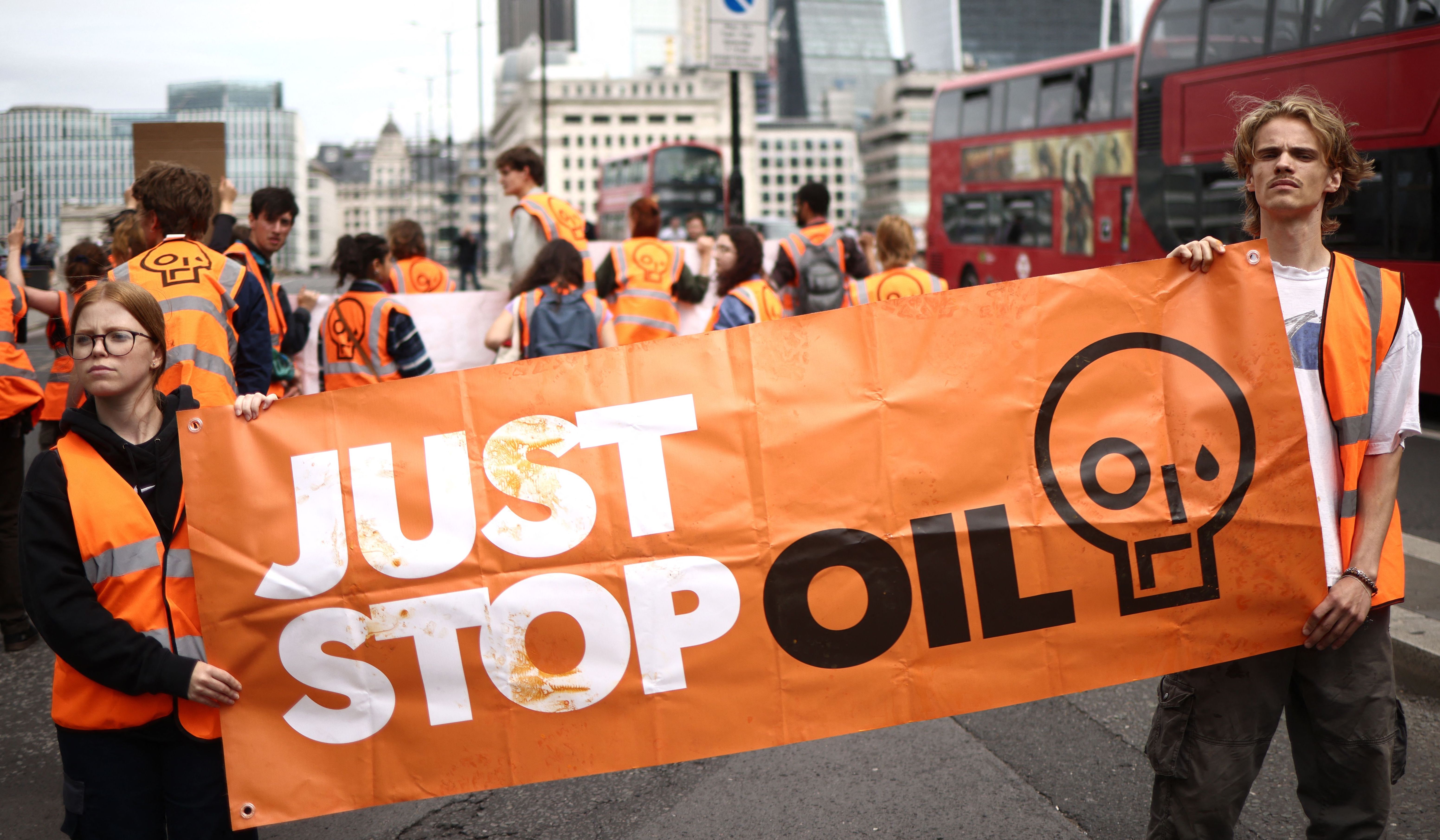Two Just Stop Oil protesters hold a large orange banner with the organisation
