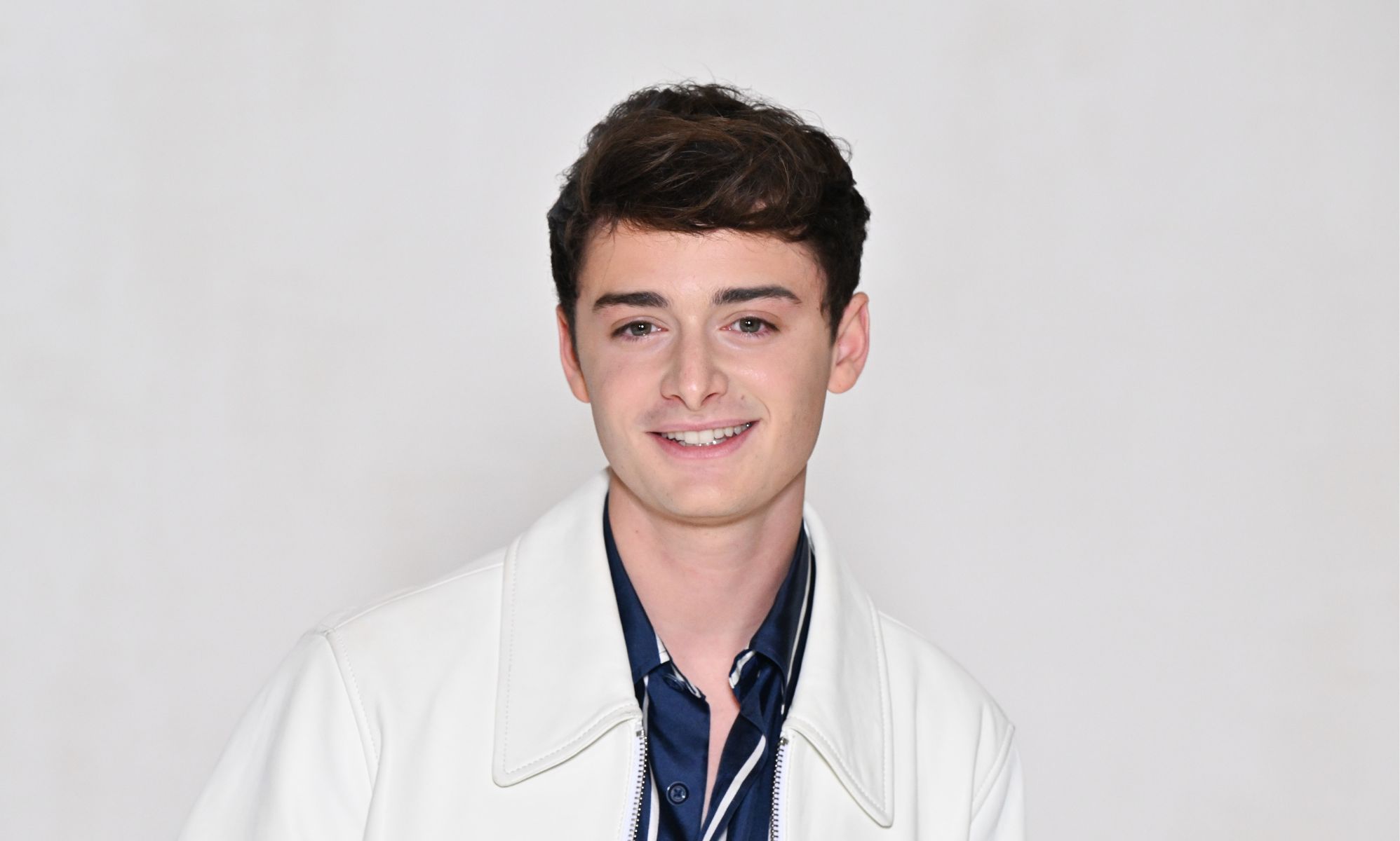 Noah Schnapp in a white blazer and blue and white pinstriped shirt.