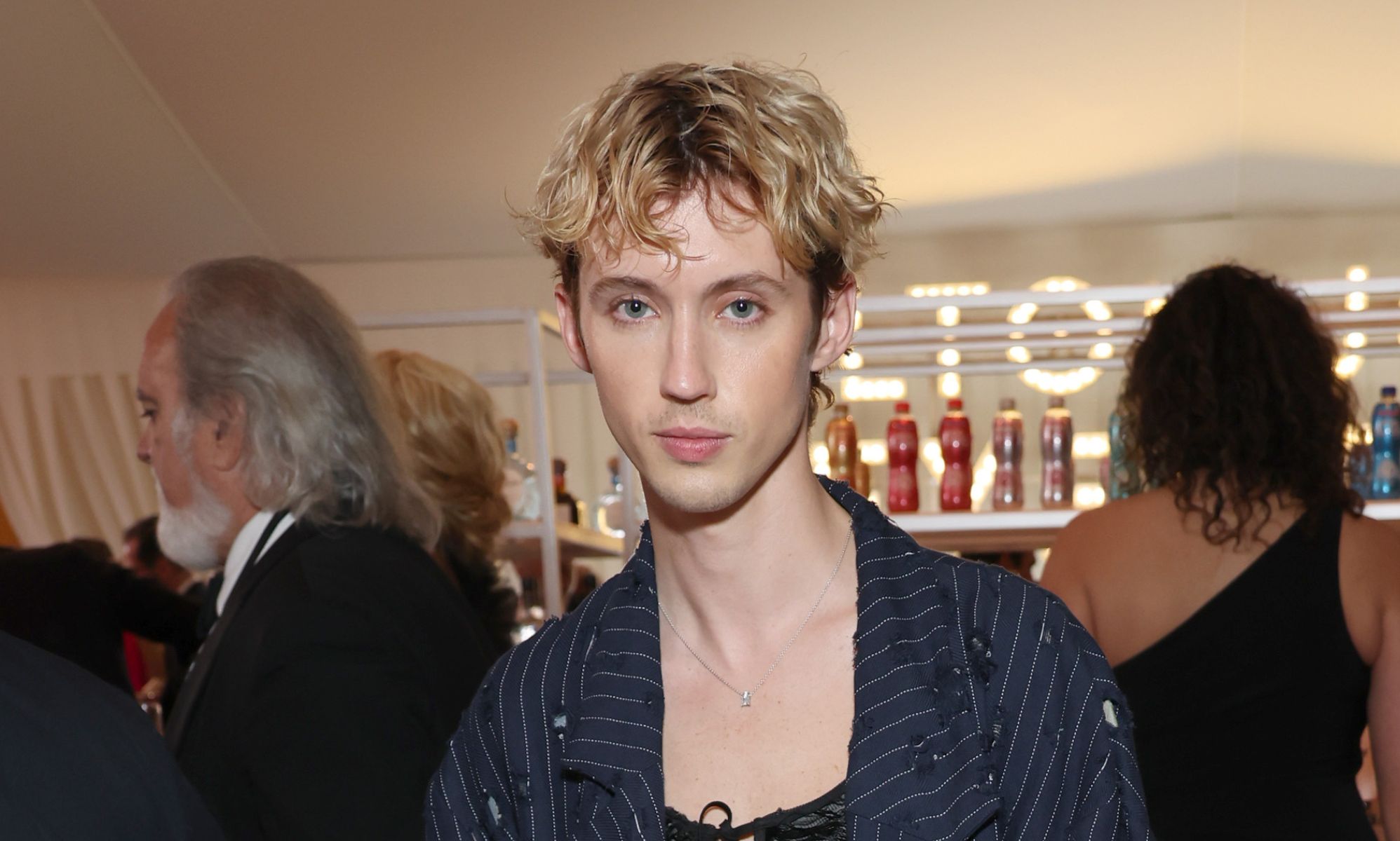 Troye Sivan wears a black pinstriped blazer and low cut top.