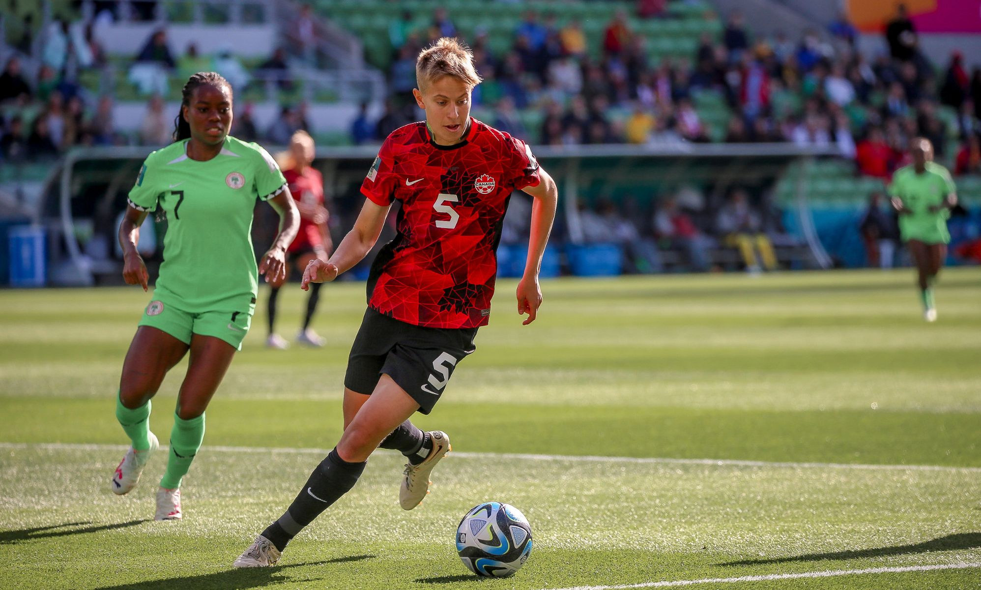 Canadian footballer Quinn wears a red and black uniform as they chase a football along the field at the 2023 Women