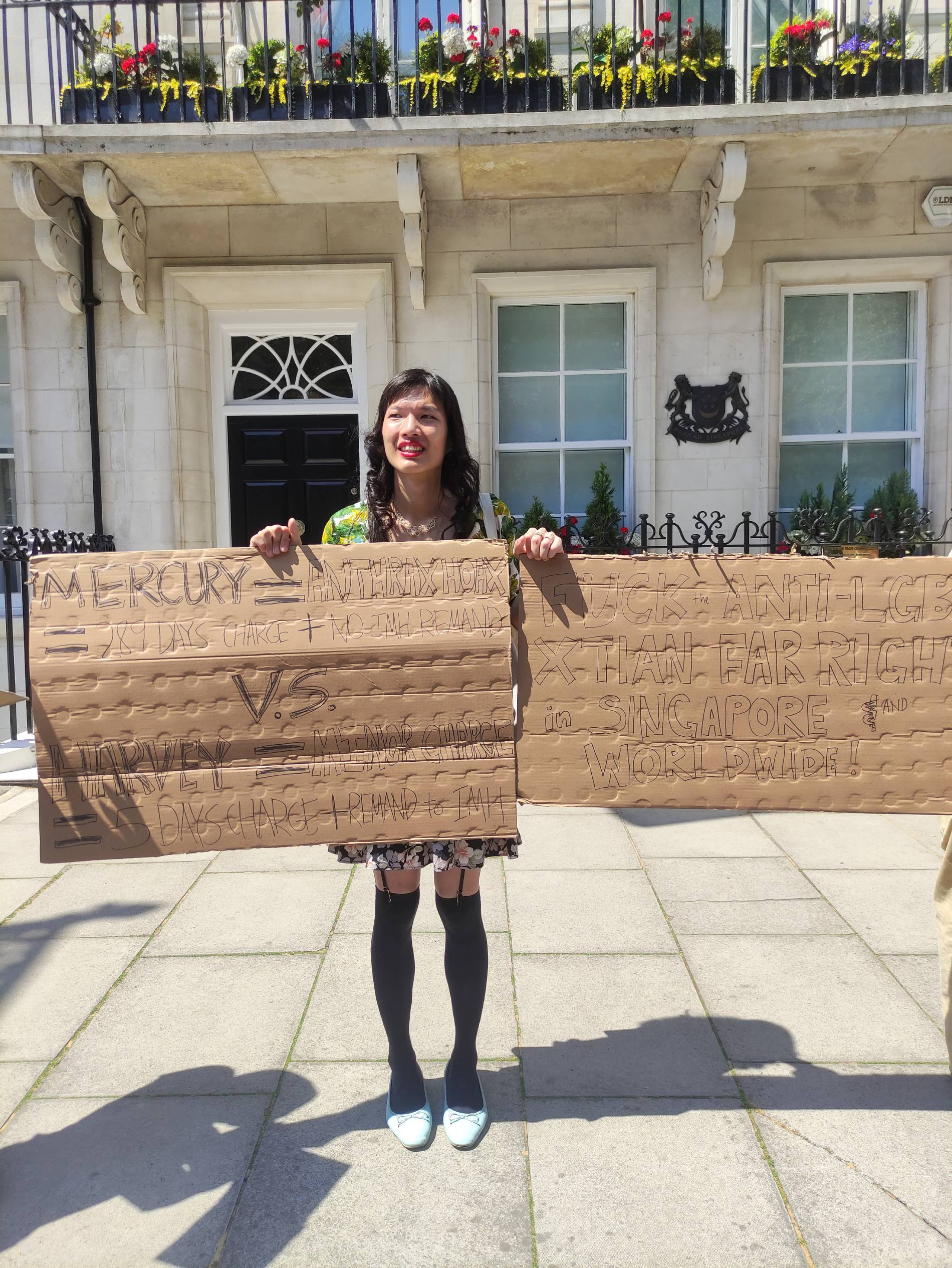 Trans woman Lune Loh holds up two cardboard signs outside the Singapore High Commission in London, UK during a protest denouncing attacks she