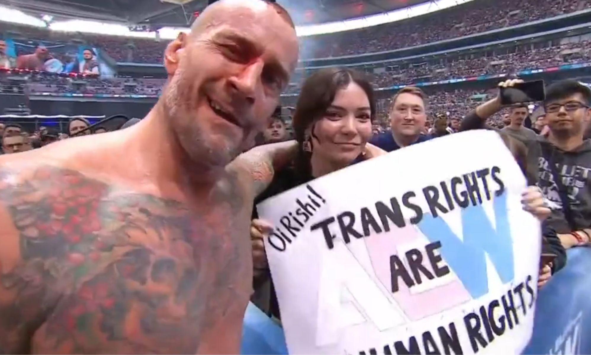 CM Punk with a fan holding a sign that reads &quot;Oi Rishi! Trans rights are human rights.&quot;