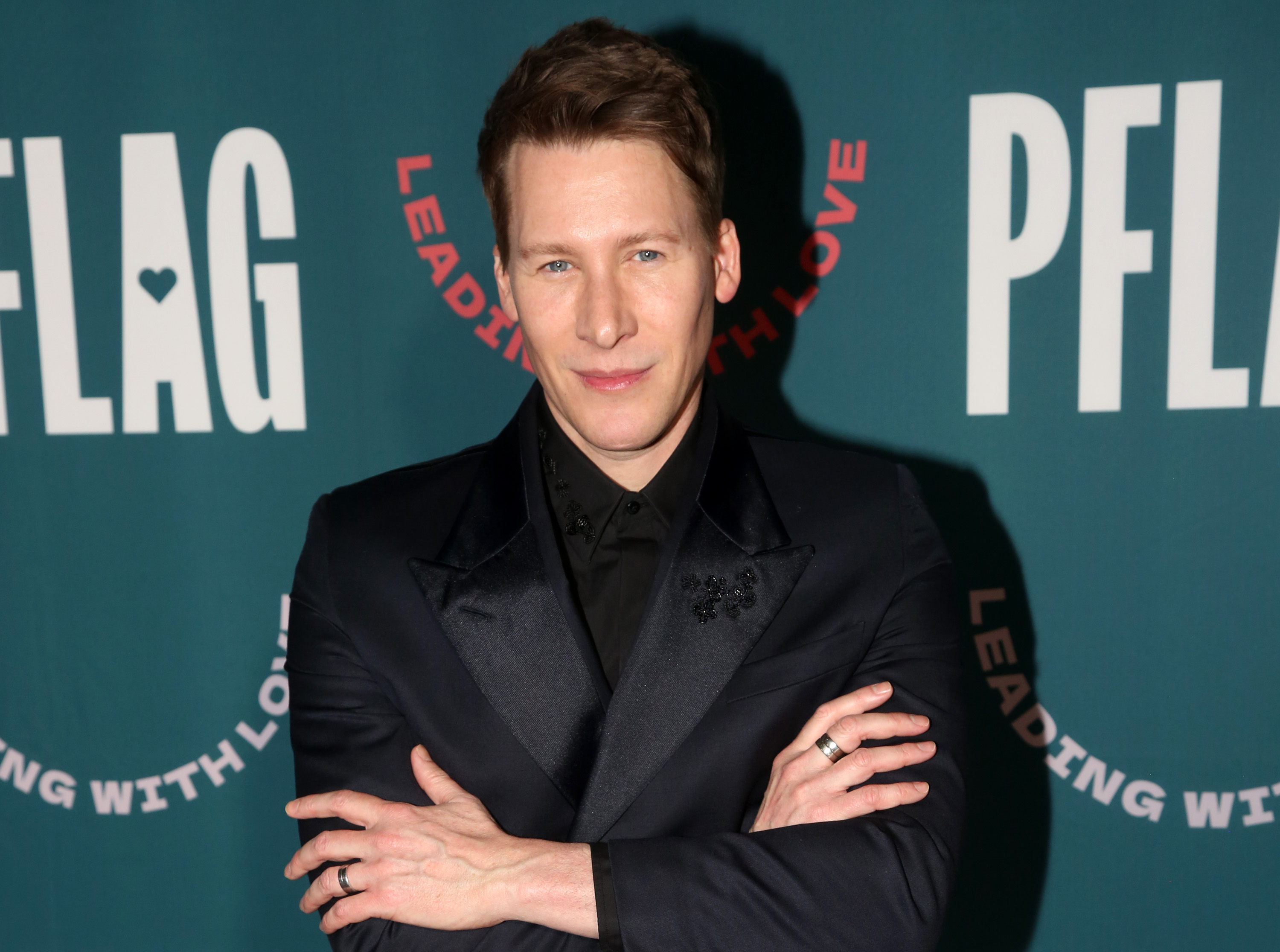 Dustin Lance Black poses on the red carpet in a black suit and shirt