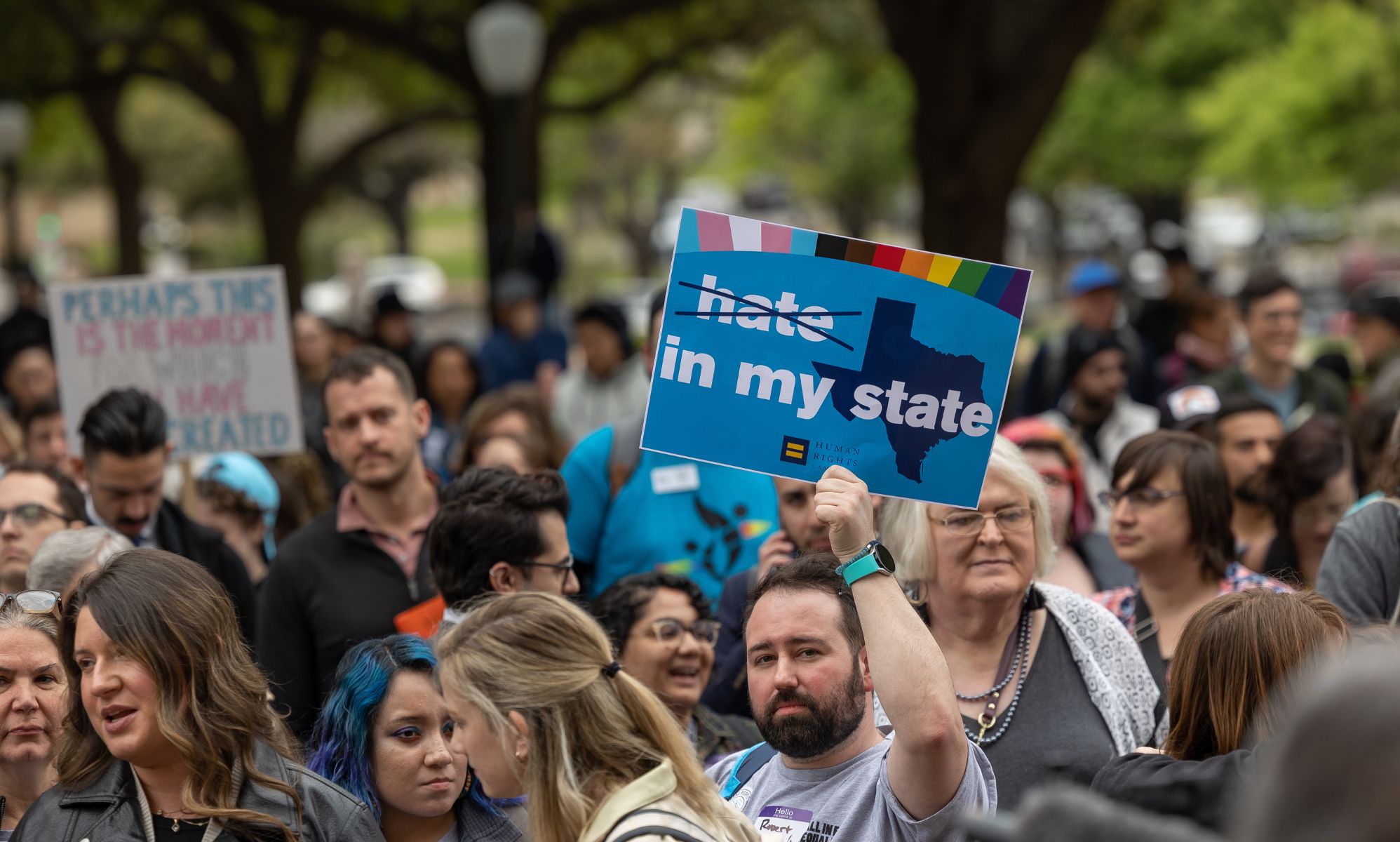 A person holds up a sign with a picture of the state of Texas on it with the words 