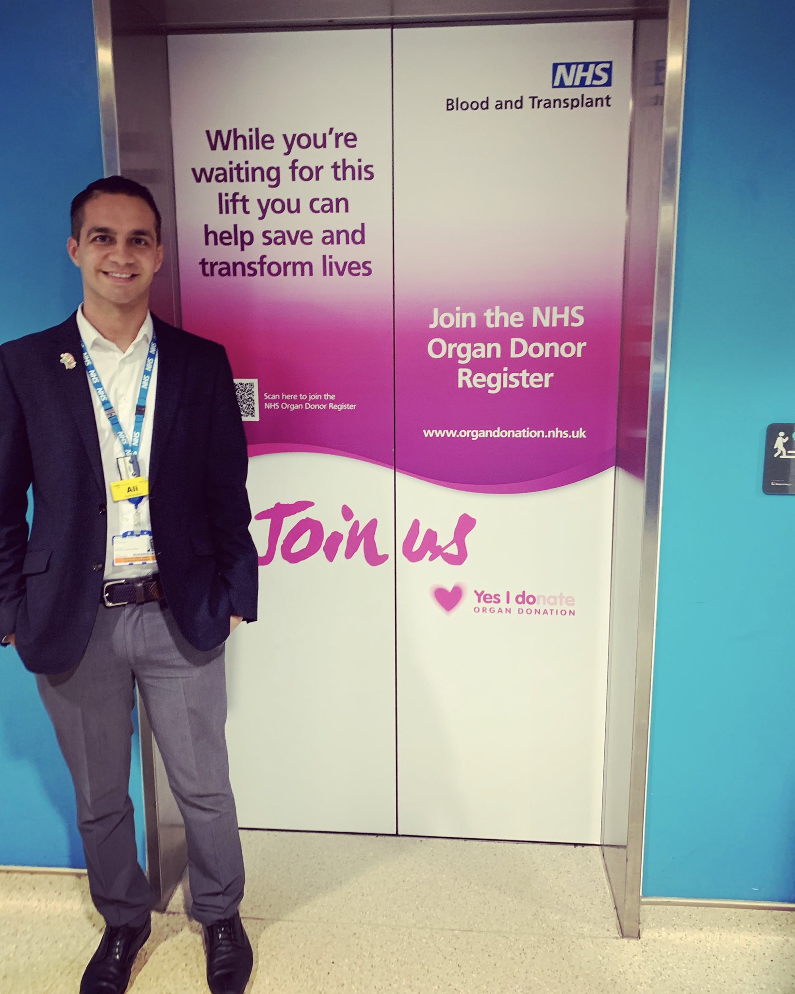 Ali Dawson pictured standing by a lift. There is writing on the lift wall which urges people to become an organ donor.