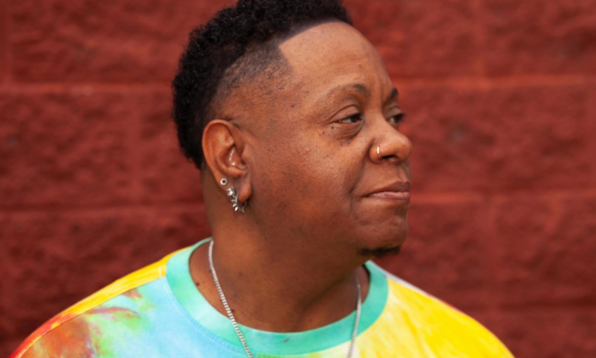 Lonnie &quot;Love&quot; Kenebrew, a trans man who came out as an elder, wears a rainbow tie dye shirt as he stares somewhere off camera