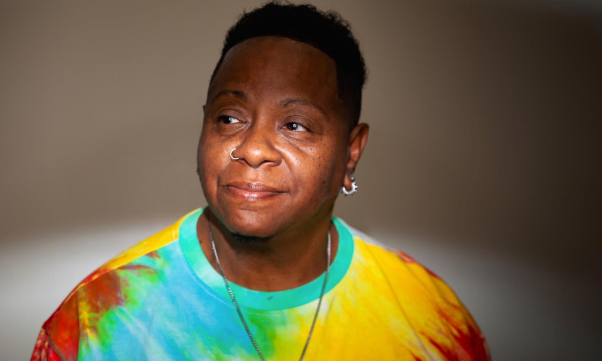 Lonnie &quot;Love&quot; Kenebrew, a trans man who came out as an elder, wears a rainbow tie dye shirt as he stares somewhere off camera
