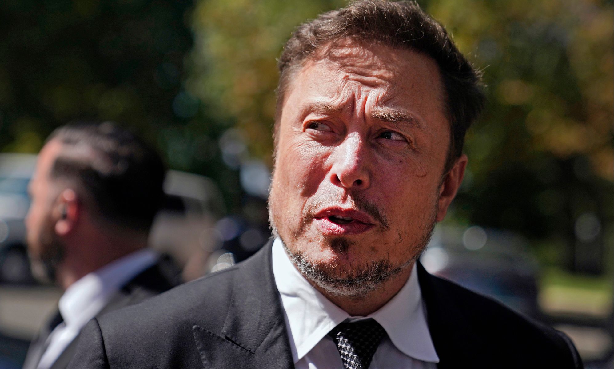 Elon Musk looking off to the right in an outdoor car park.