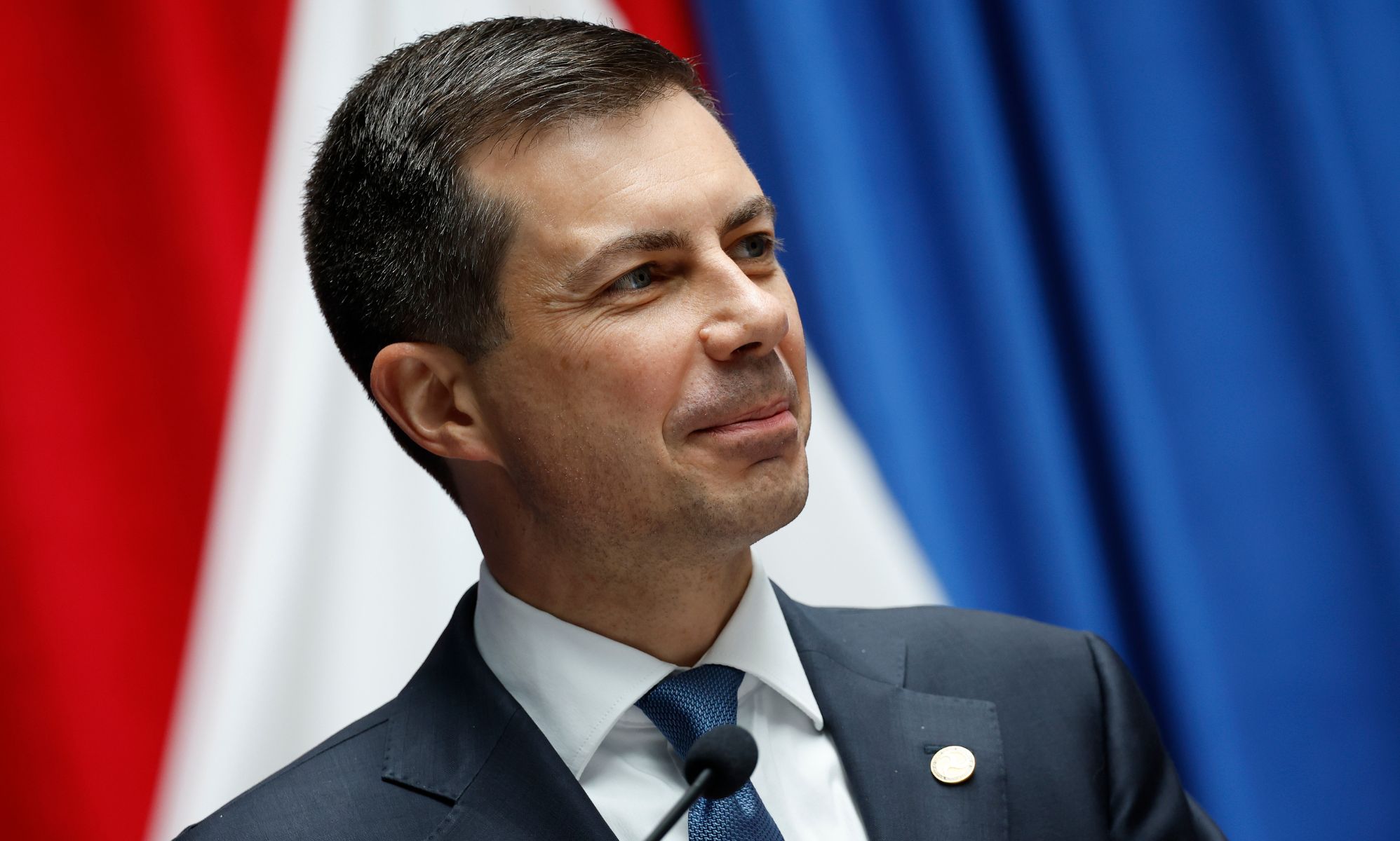 Pete Buttigieg smiling while on the stand of a press conference stage.