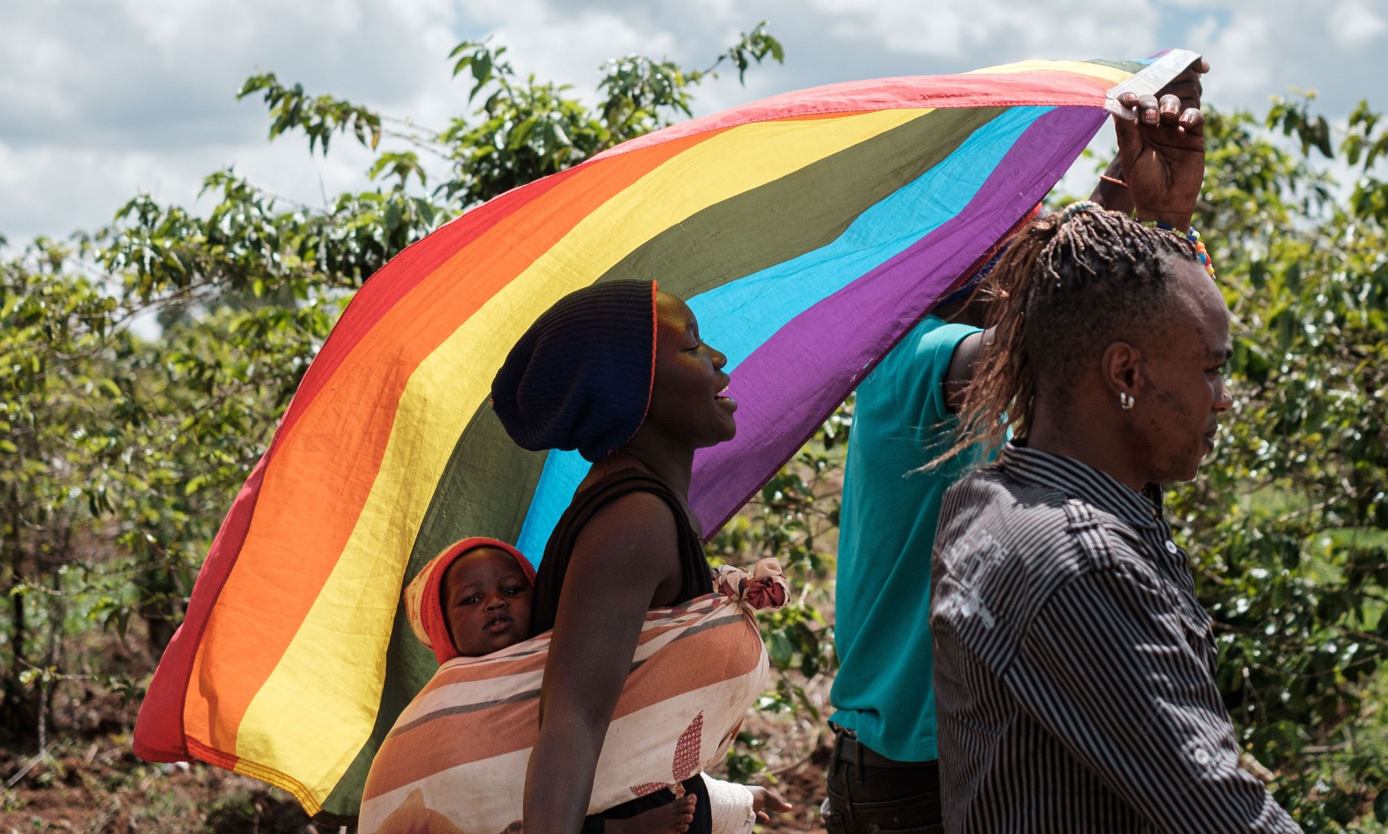LGBTQ+ refugees from Uganda and other African countries walk together outside while they are living in Kenya and waving a rainbow flag