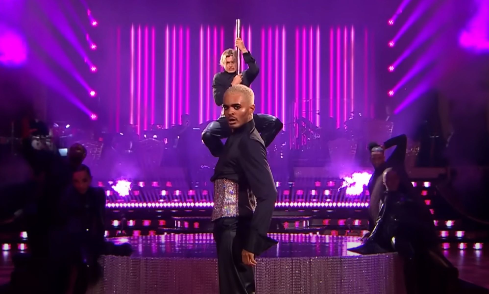 Layton Williams and Nikita Kuzmin wear matching sparkly corsets and black outfits as Williams stands in front of Kuzmin, who is clutching a pole, during a performance on BBC
