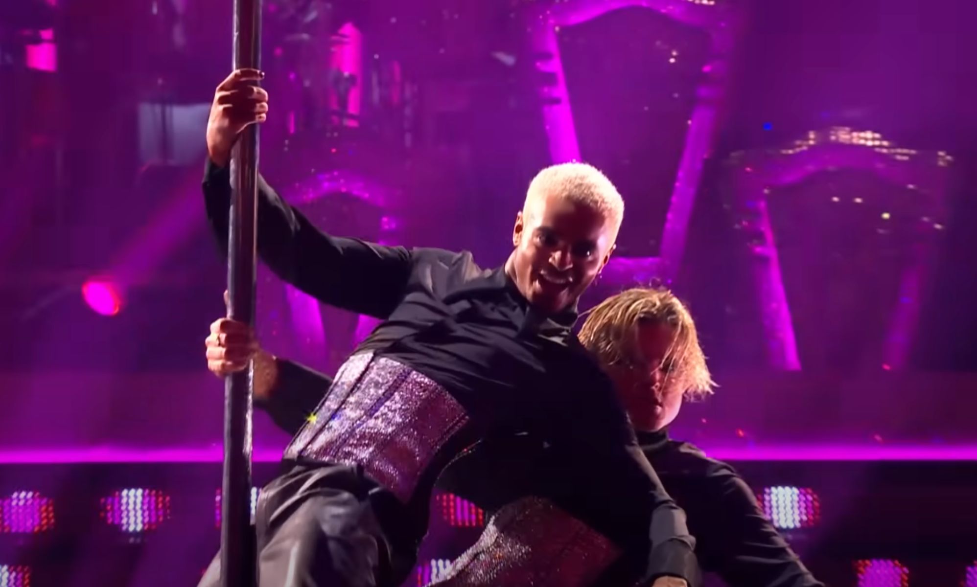 Layton Williams and Nikita Kuzmin wear matching sparkly corsets and black outfits as they clutch a pole during a performance on BBC