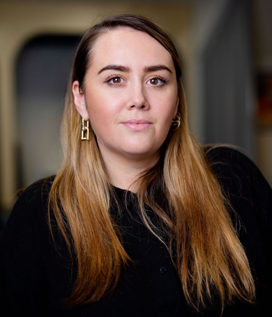 This is an image of a white woman. She has long dark blond hair. she is wearing dangly earrings and is wearing black.