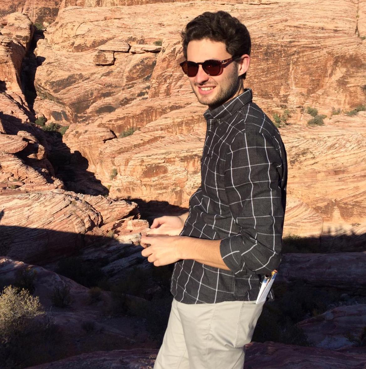 This is an image of a white man standing outside. He has dark hair and is wearing dark sunglasses.