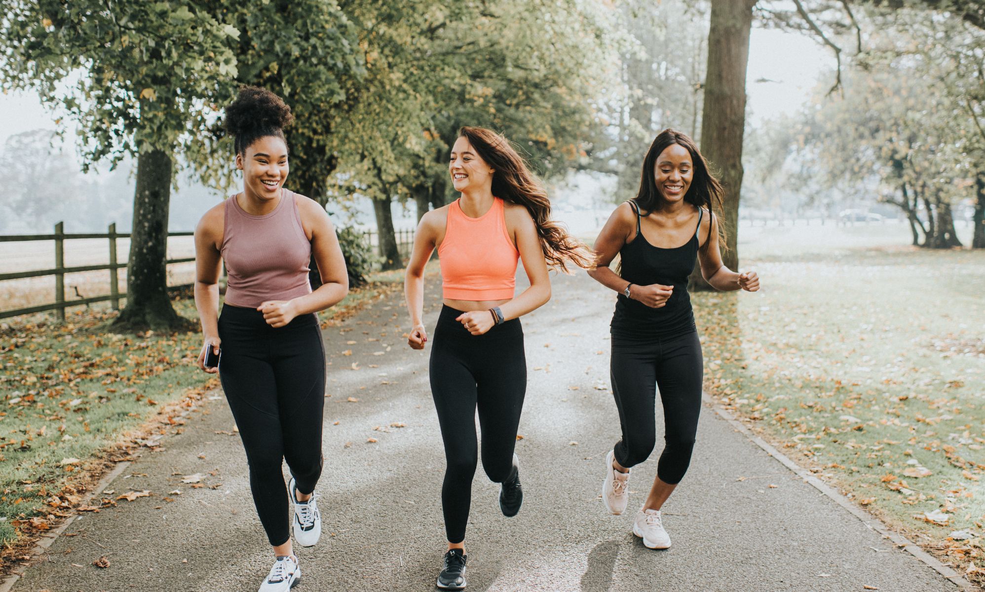Three female presenting people running in the woods and smiling