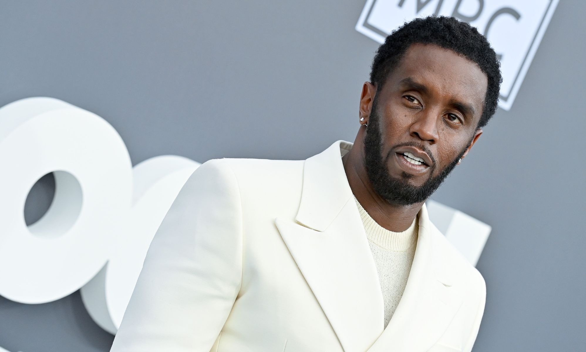 Music mogul Sean &quot;Diddy&quot; Combs wears a white shirt and matching suit while posing for a picture at an event