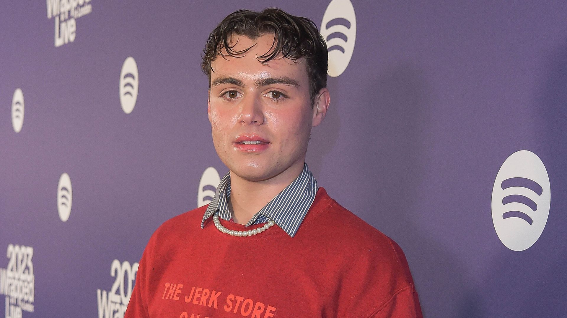 Heartstopper star Bradley Riches wears a red jumper with gelled hair