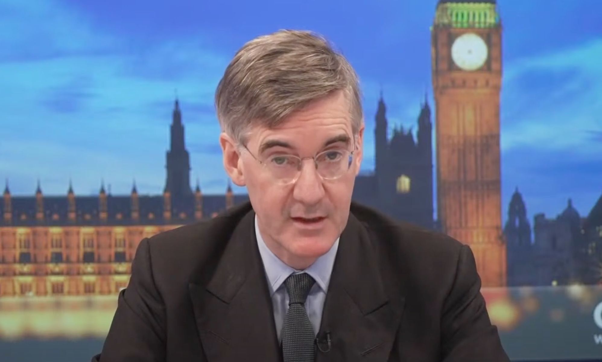 Tory MP Jacob Rees-Mogg sits at the desk as he presents on GB News