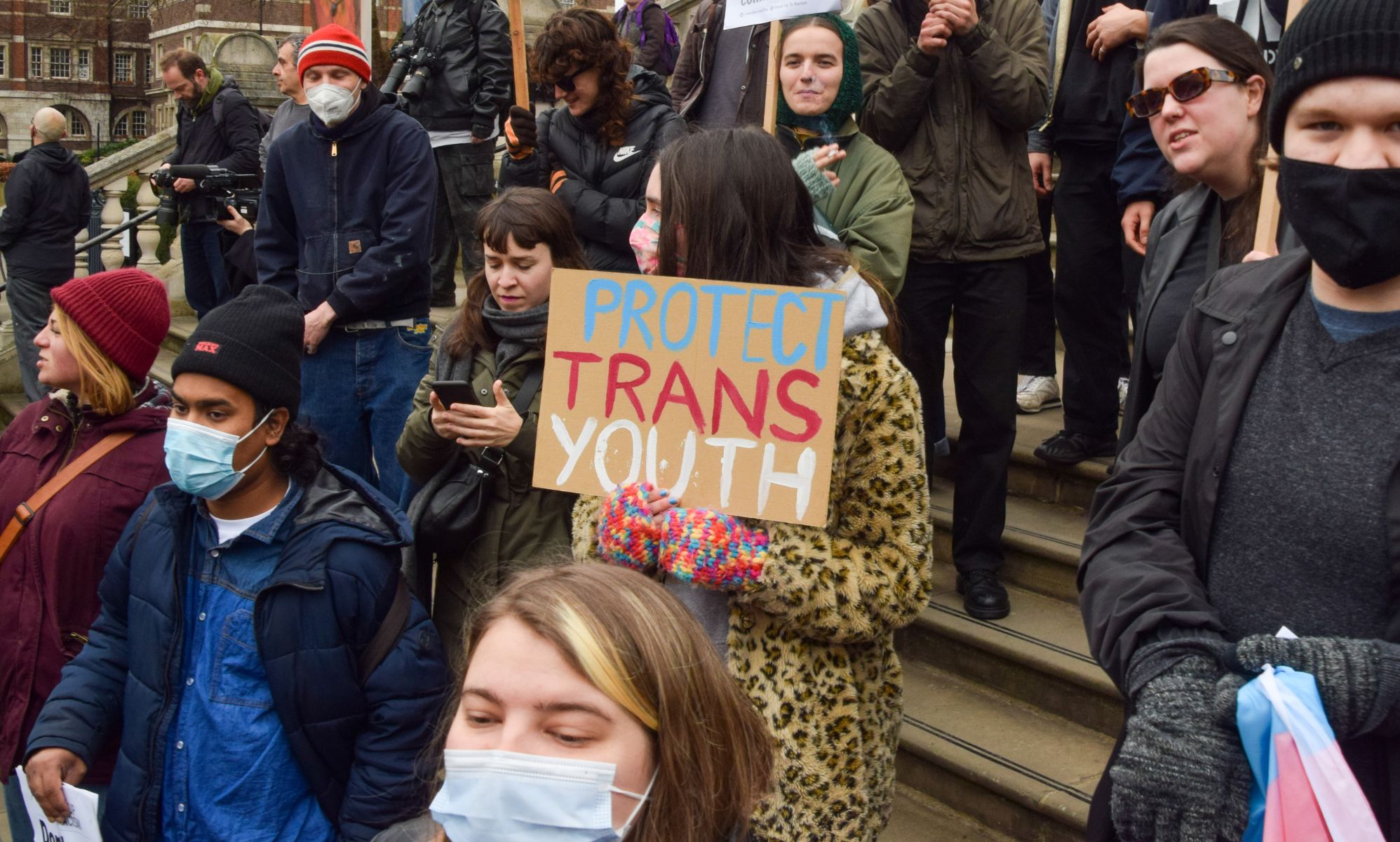 Activists in a crowd hold signs, with one saying &quot;protect trans youth.&quot;