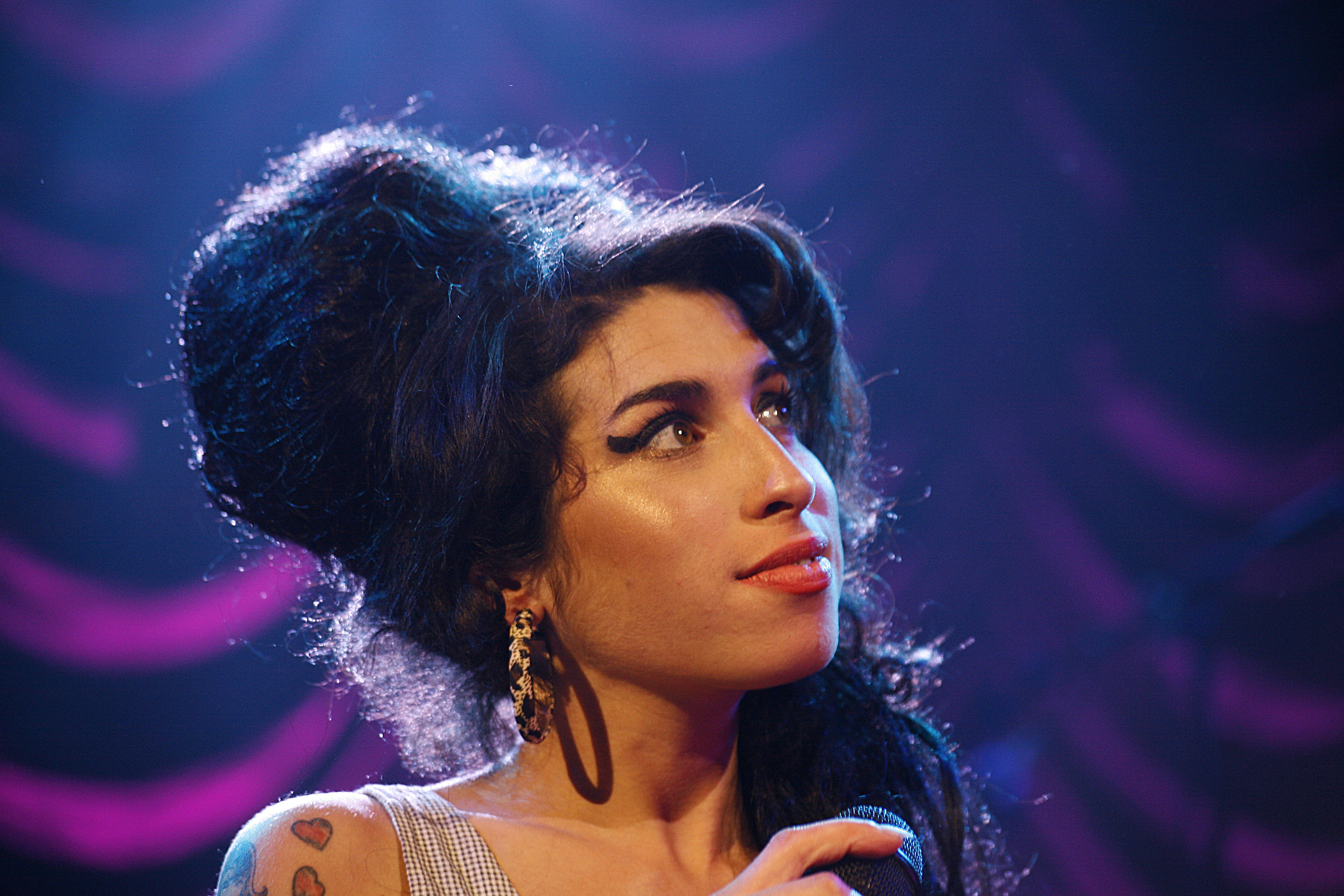 Amy Winehouse looks off to the left while holding a microphone.
