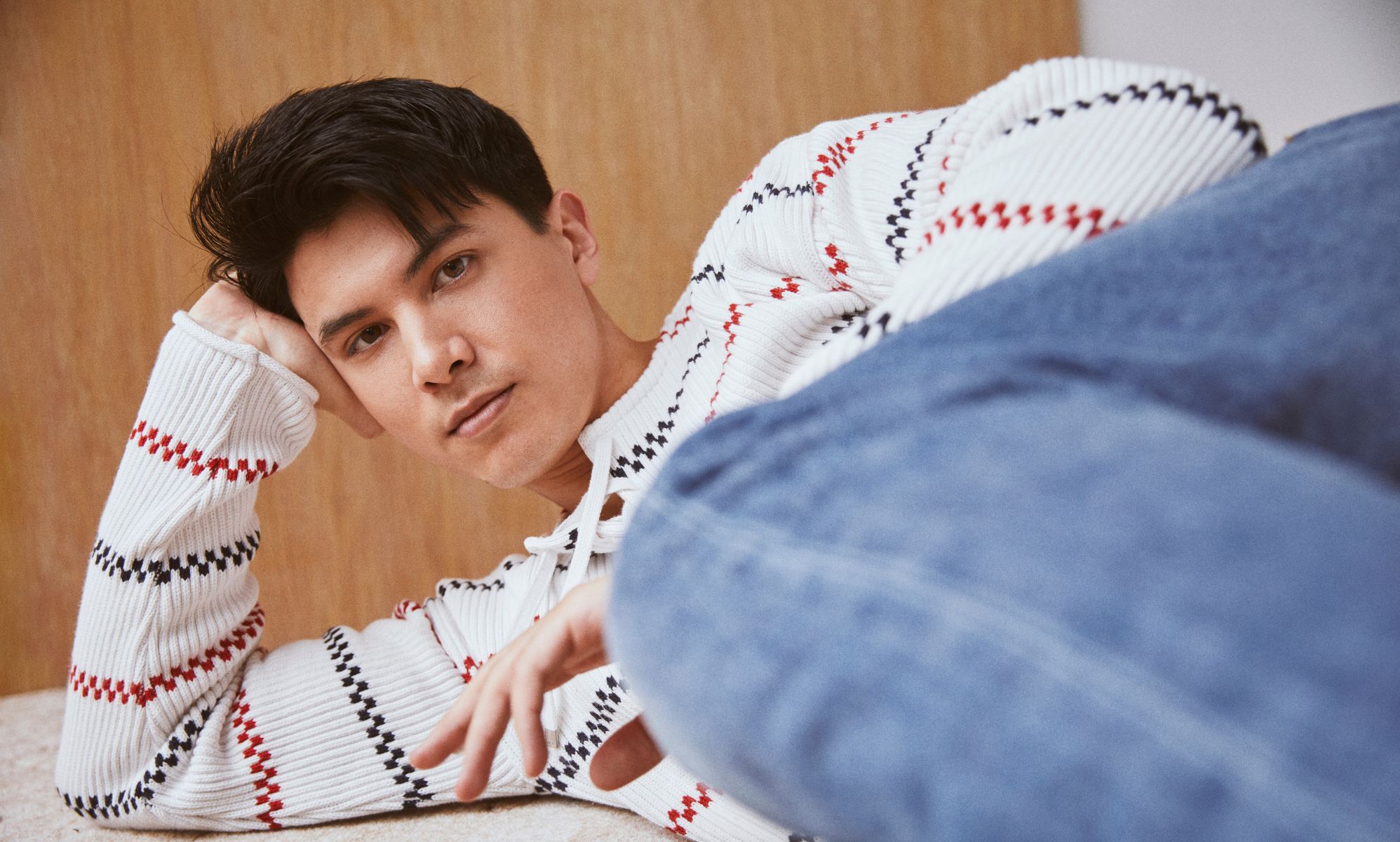 James Phoon in a white striped jumper and blue jeans, laying down on the floor.