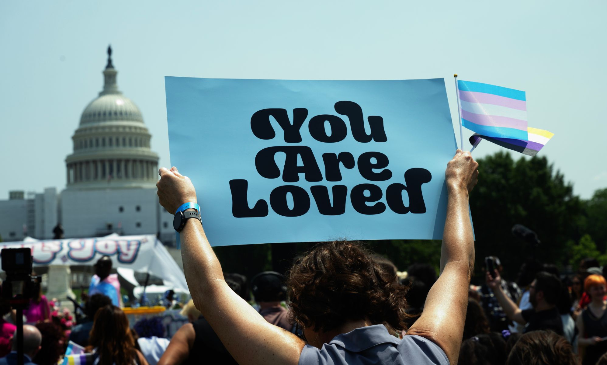 Trans youth hold up a sign reading &quot;you are loved&quot; during a protest.