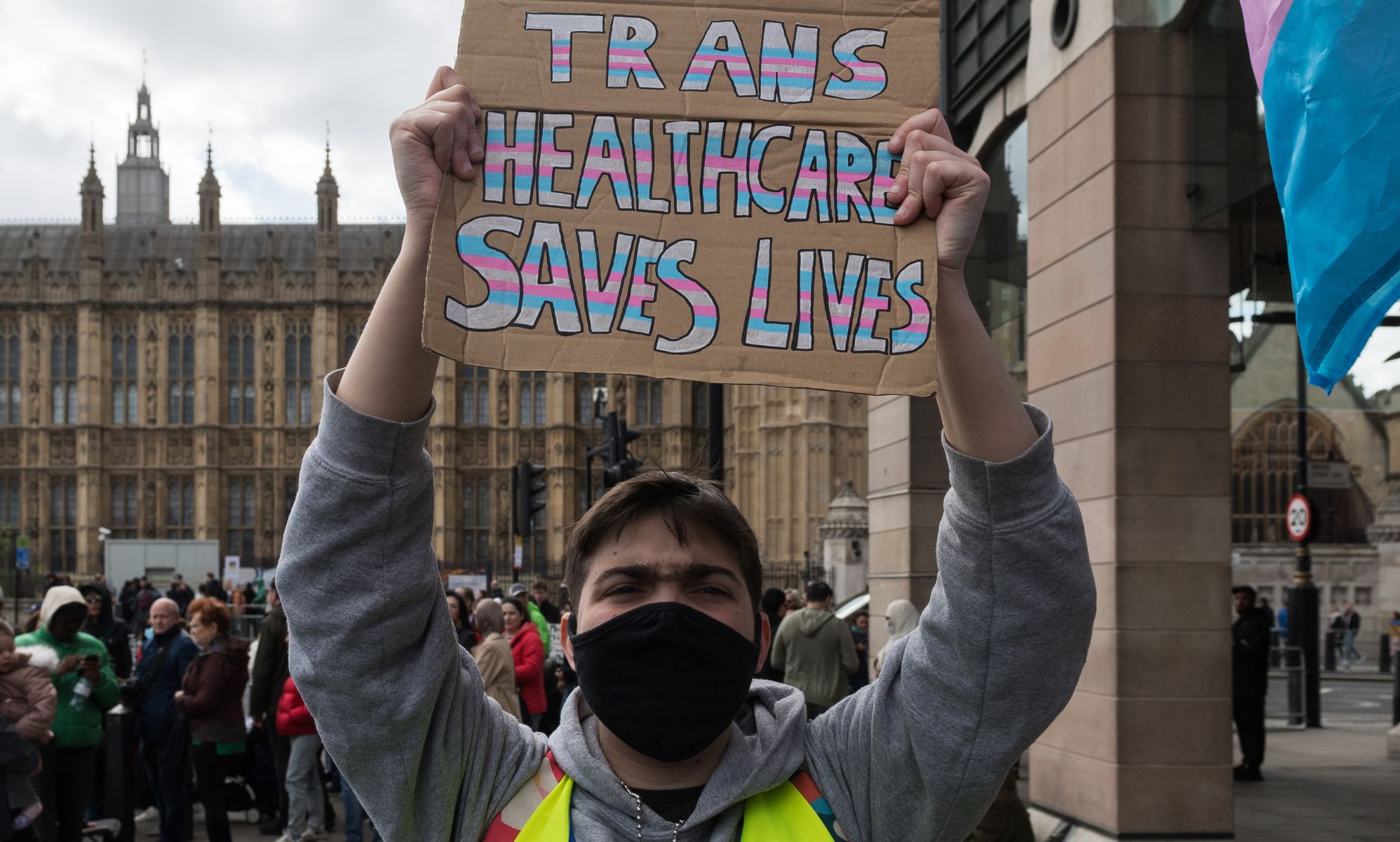 A person holding a sign that reads &quot;trans healthcare saves lives.&quot;
