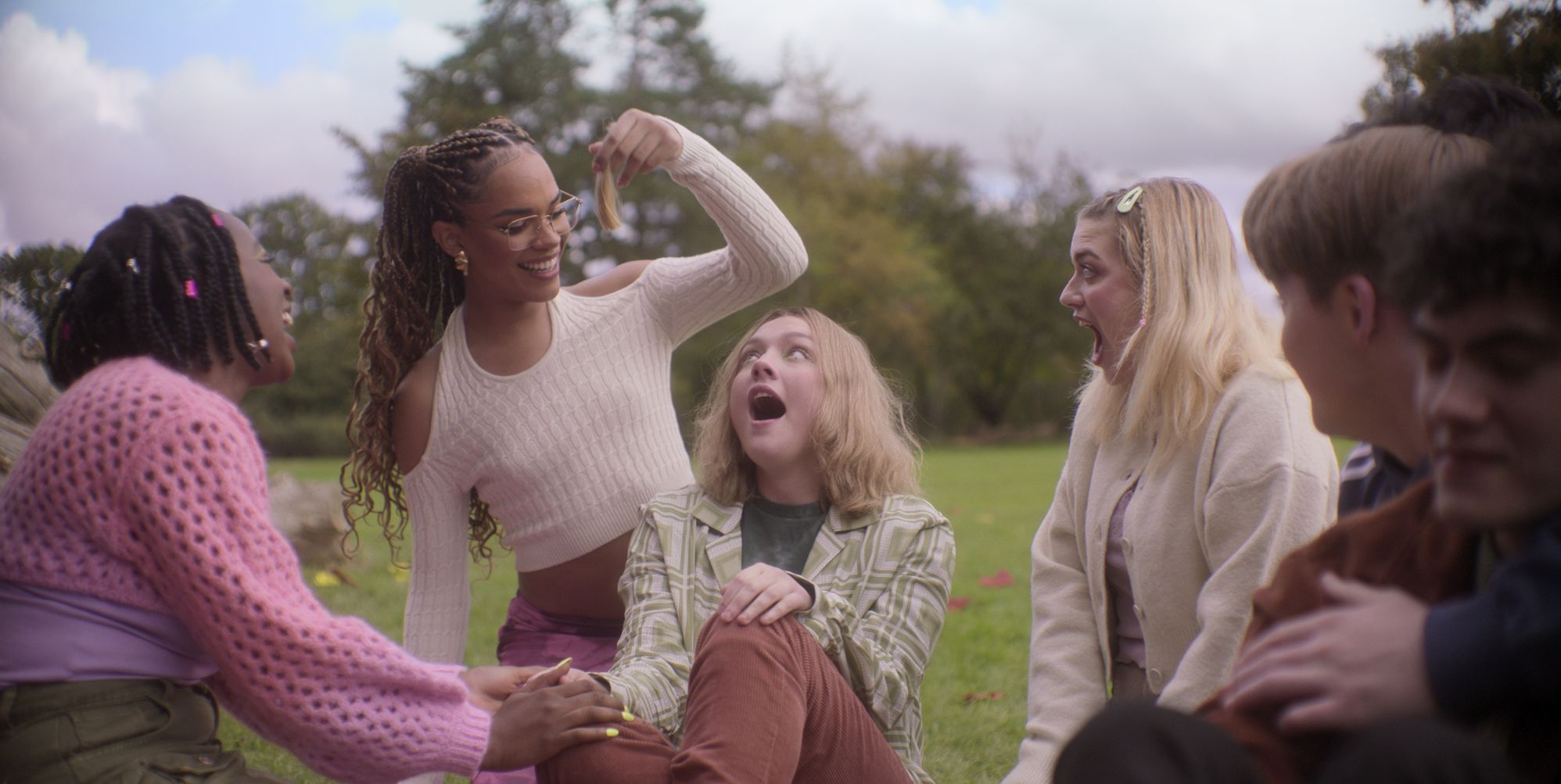 A still from Heartstopper season three featuring Darcy having their hair cut by friends.