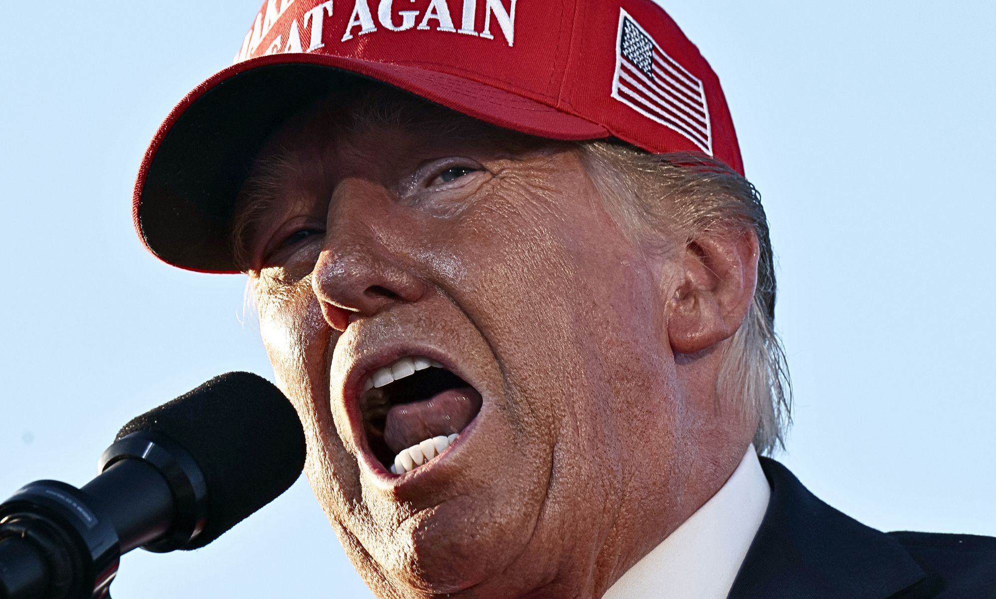 Donald Trump speaking with his mouth open into a microphone.