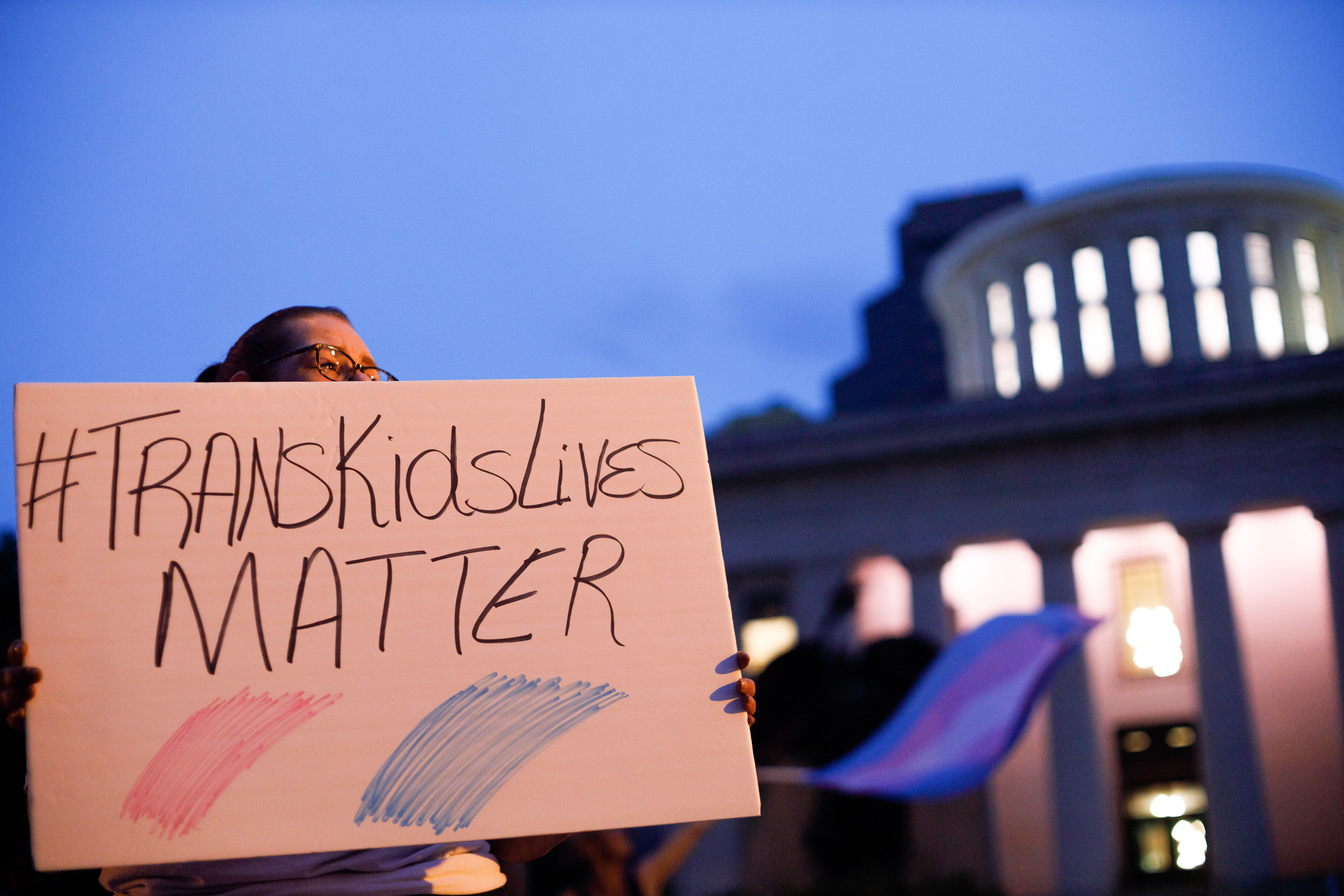 Trans rights activist holding sign which reads, &quot;Trans kids lives matter&quot;.