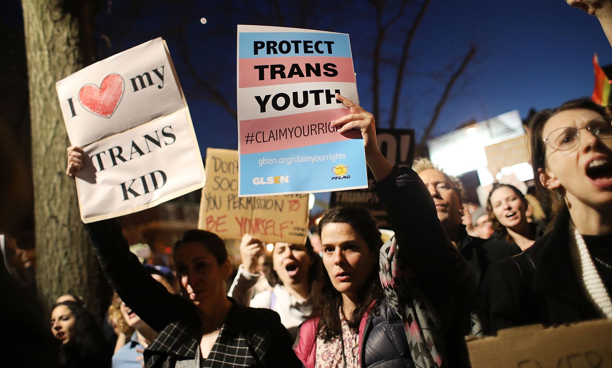 Protestors holding signs that call to protect trans youth.