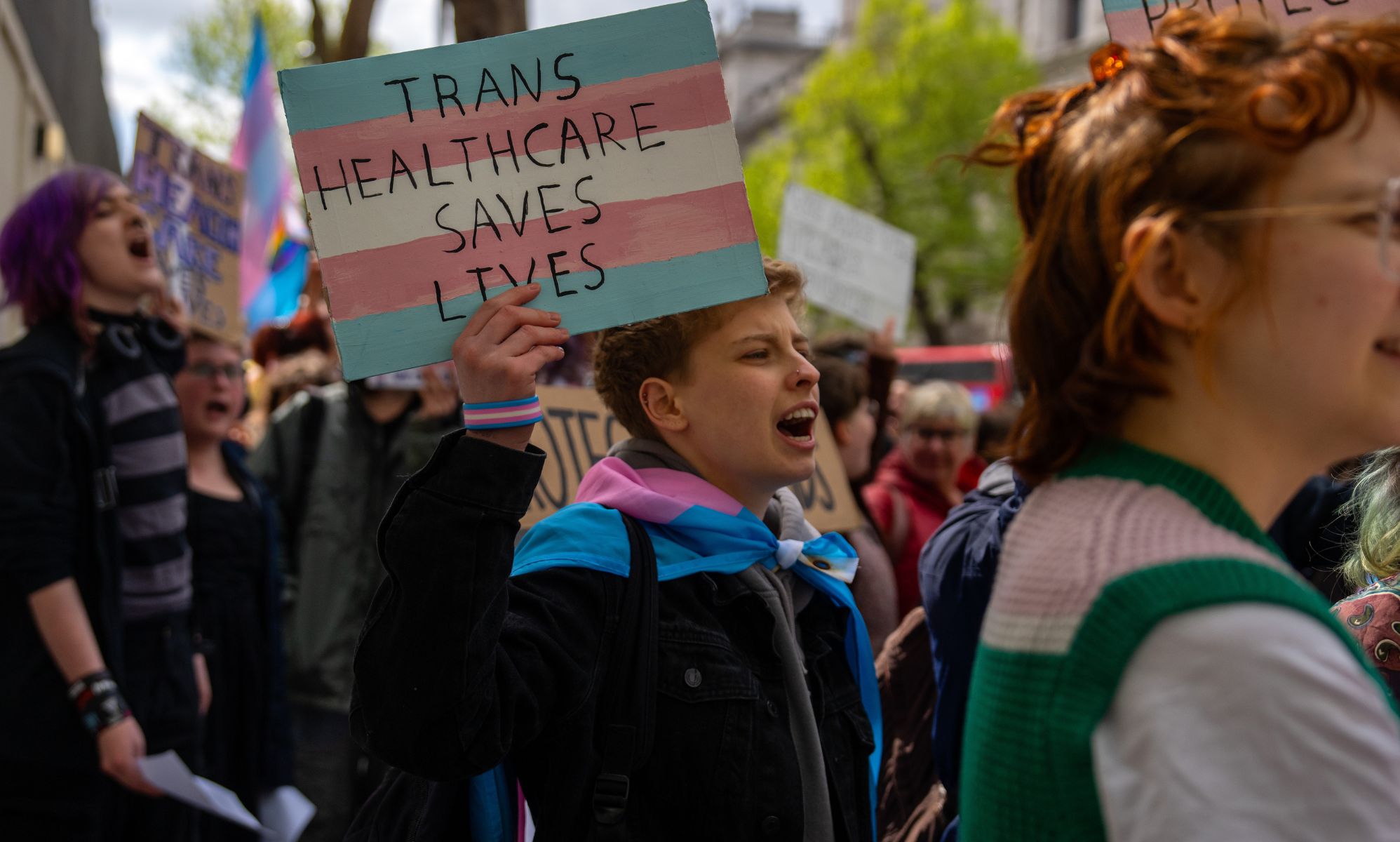 Protestors holding signs that read &quot;trans healthcare saves lives.&quot;