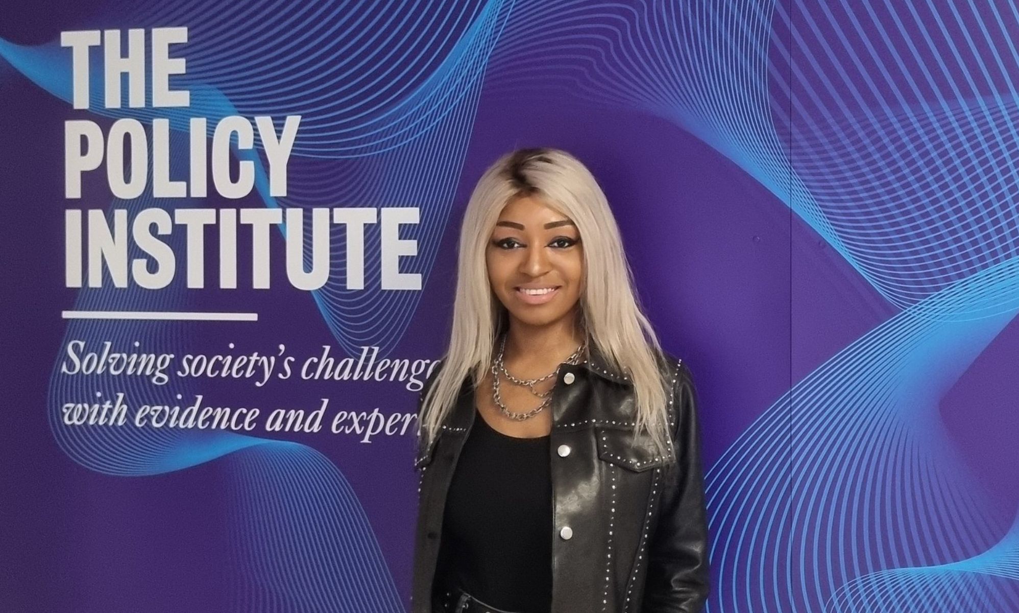 Yasmin Benoit standing next to a wall with text that reads &quot;The Policy Institute: Solving society