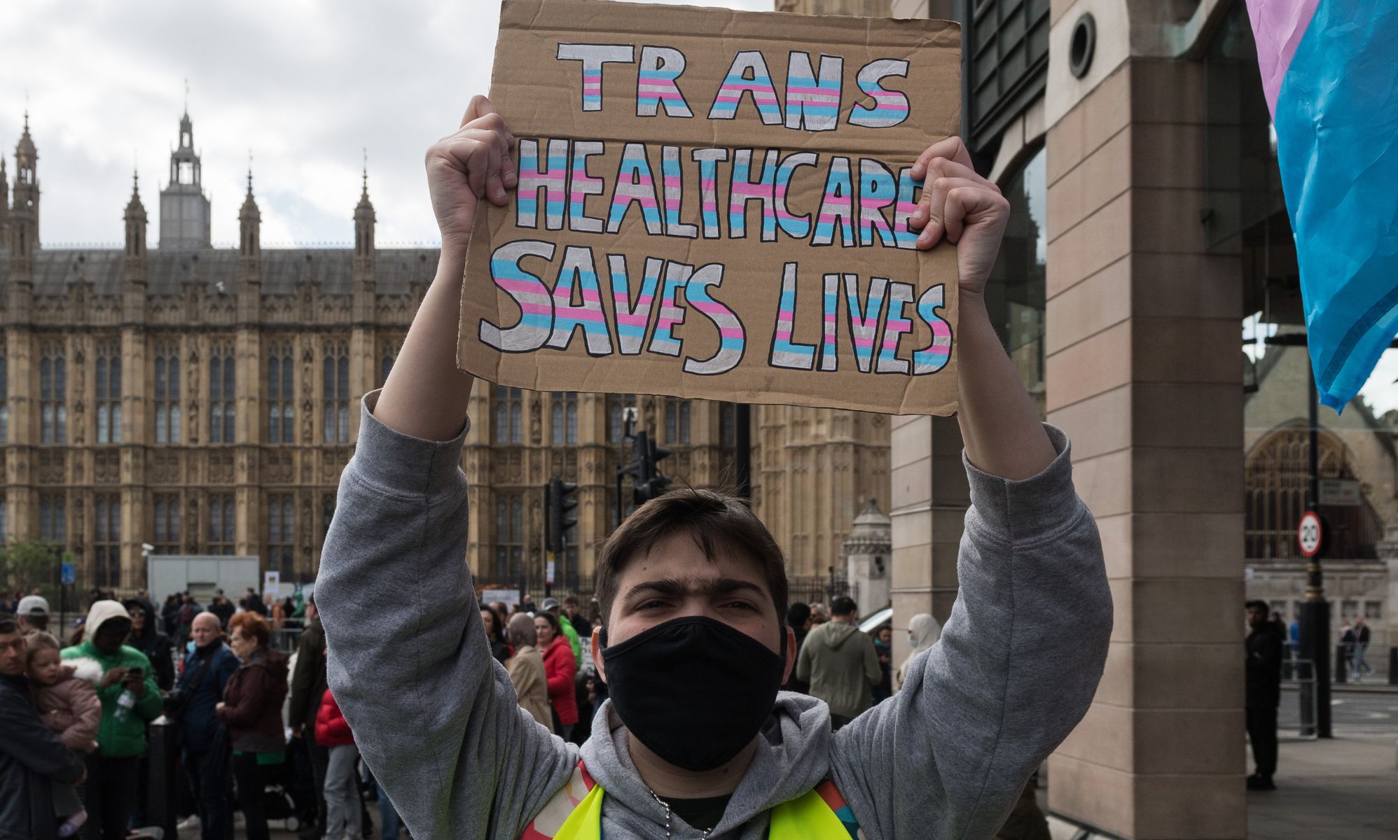 A person holds a sign reading &quot;trans healthcare saves lives.&quot;