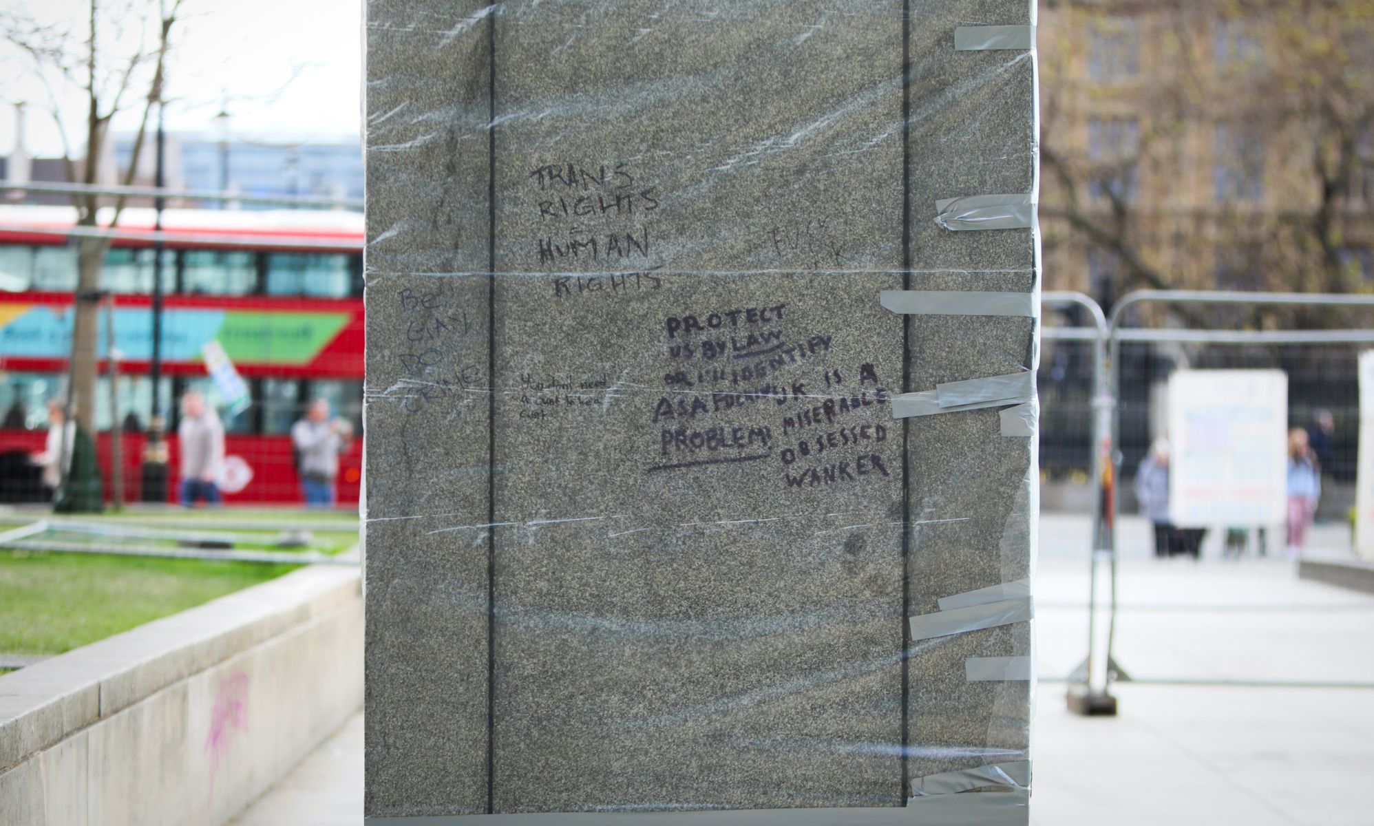 Protective film wrapped over the base of a statue where trans rights slogans have been tagged. 