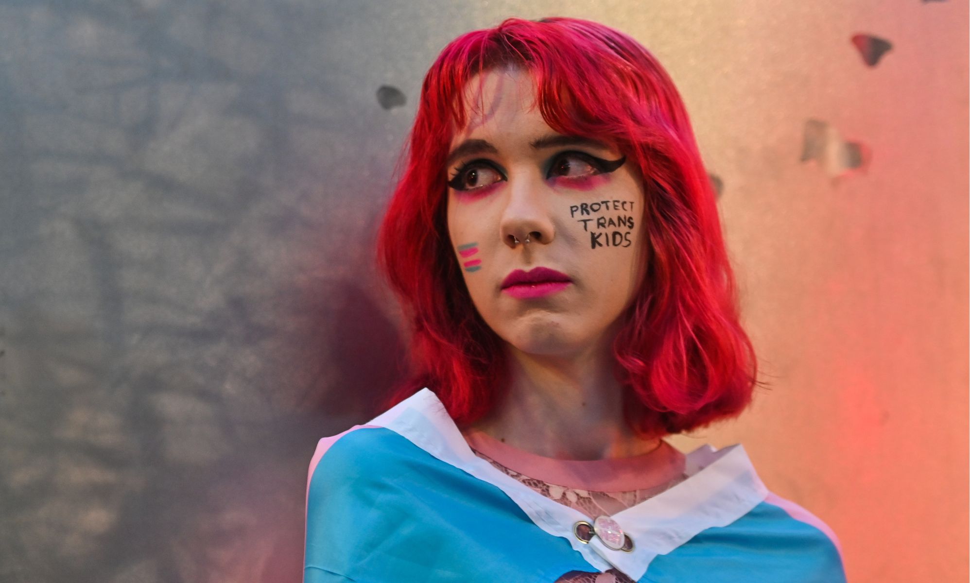 A person with face-paint reading &quot;Protect Trans Kids.&quot;