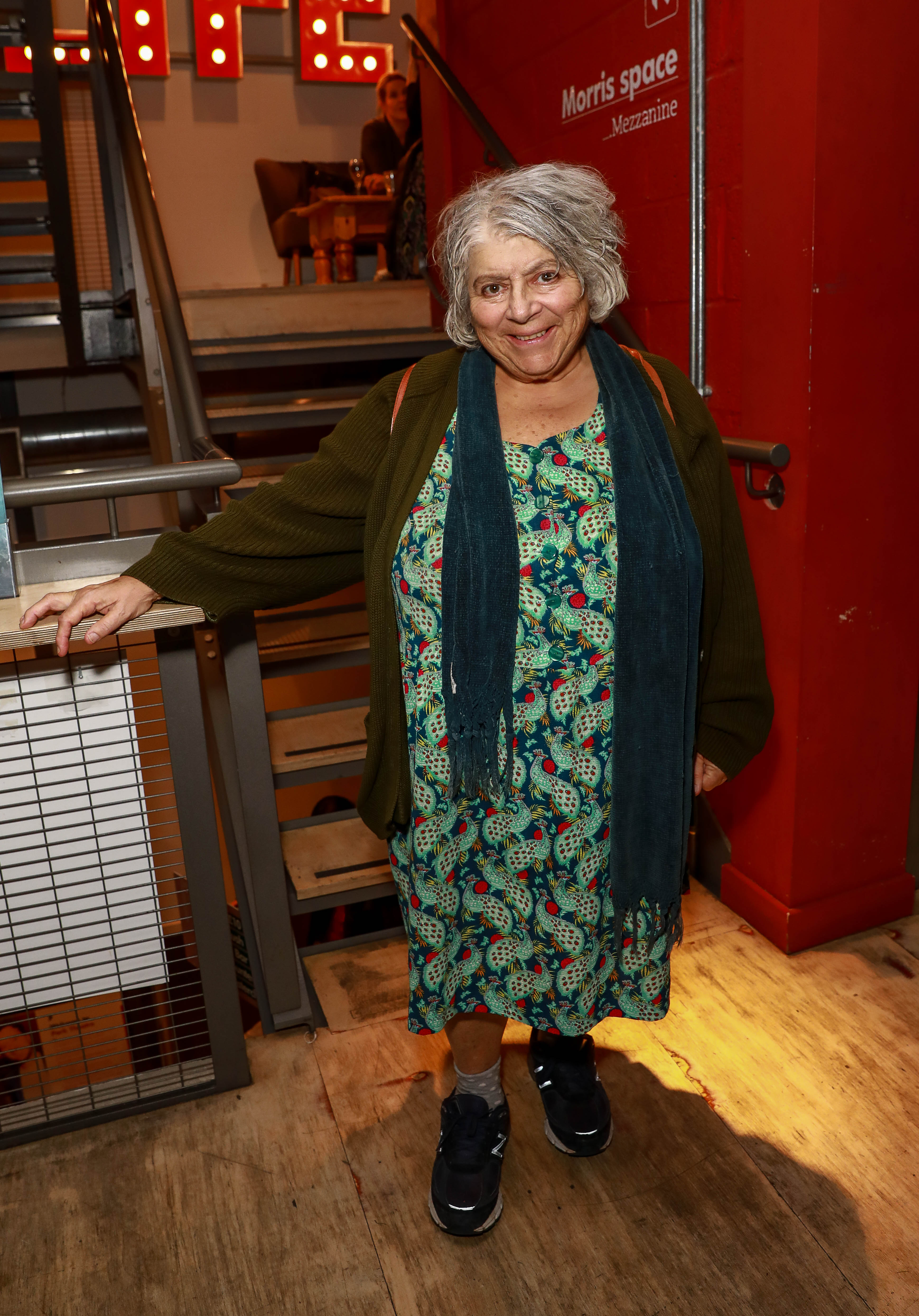 Miriam Margolyes smiling, wearing a green patterned dress with a dark green cardigan