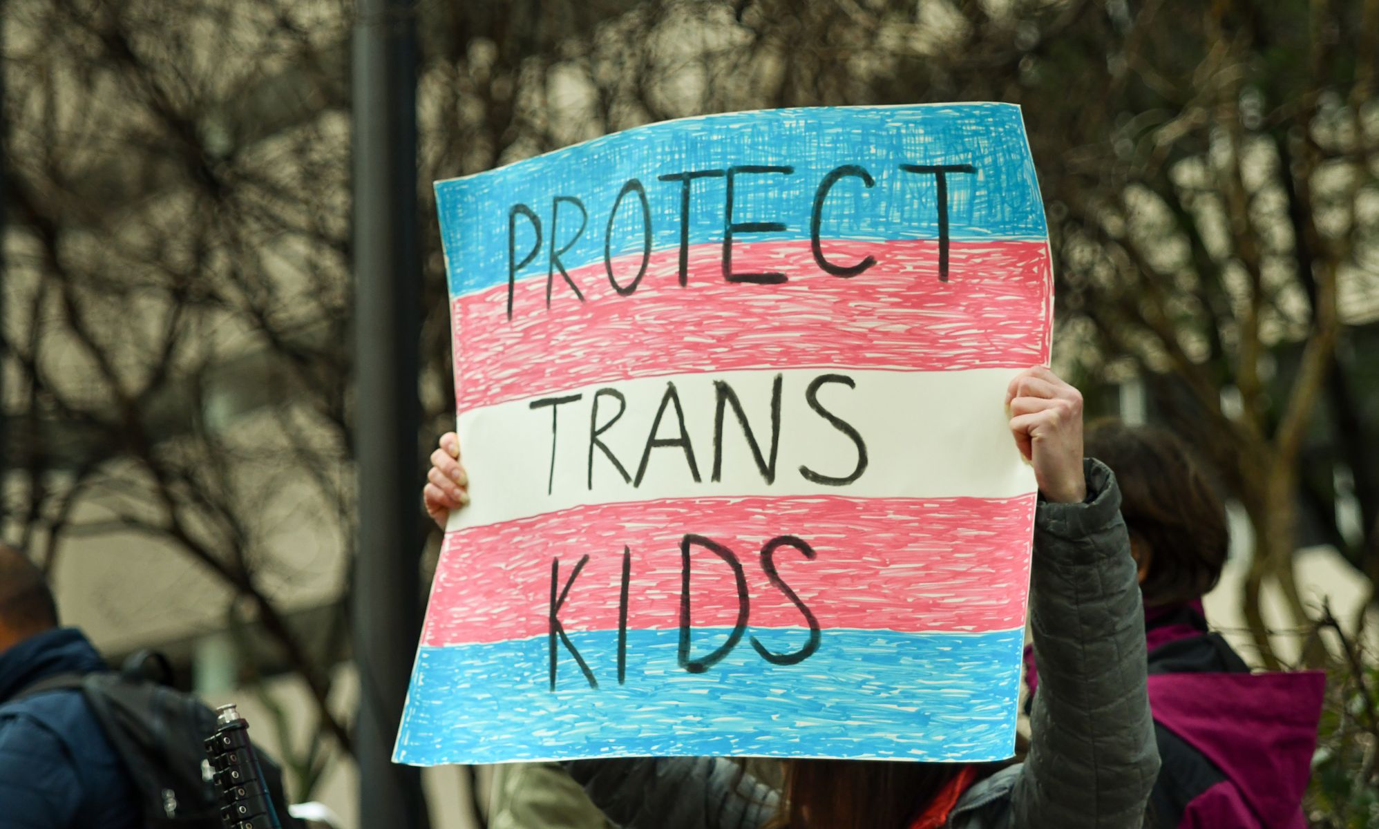 A trans person holds up a sign reading 