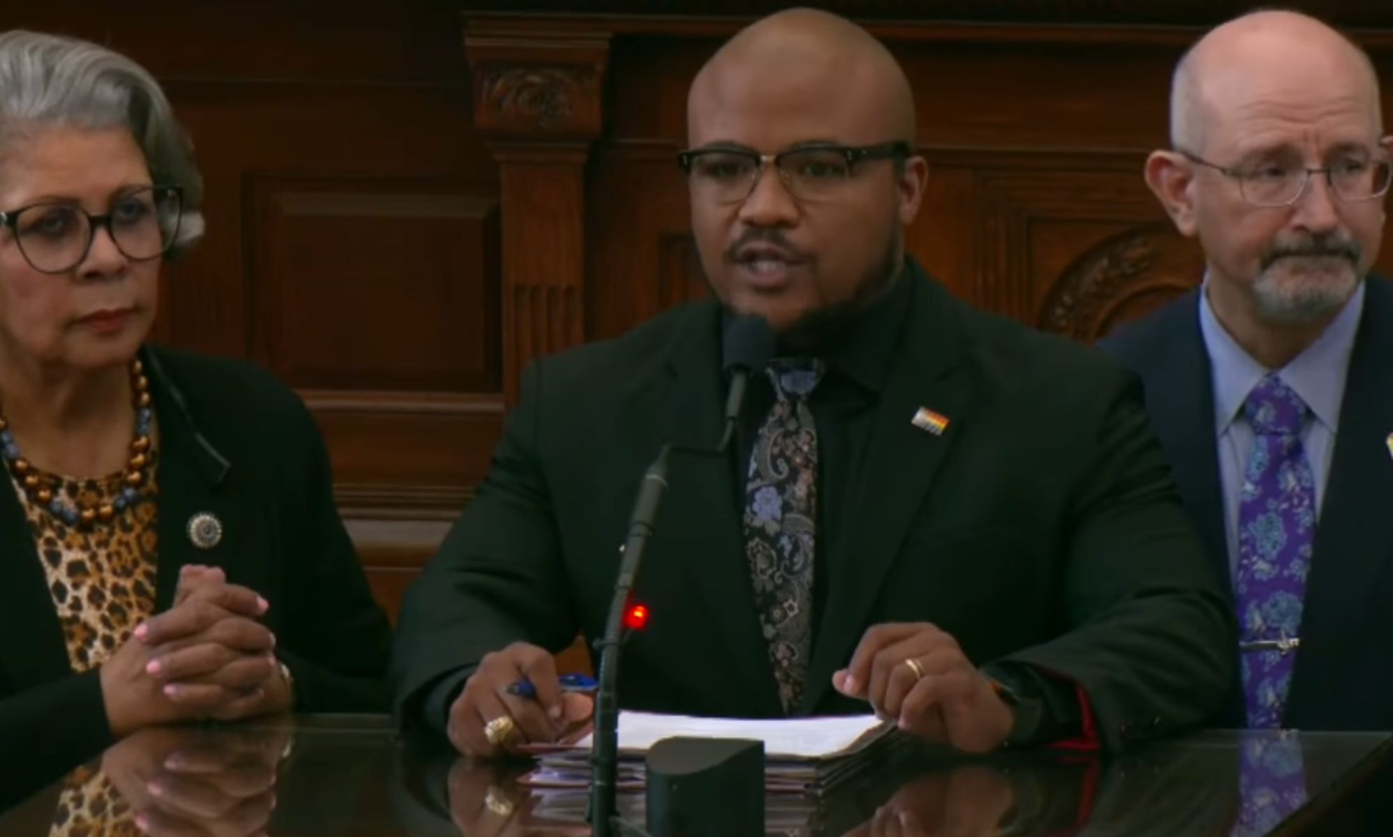 Three individuals stood at a podium in the Texas State House floor.