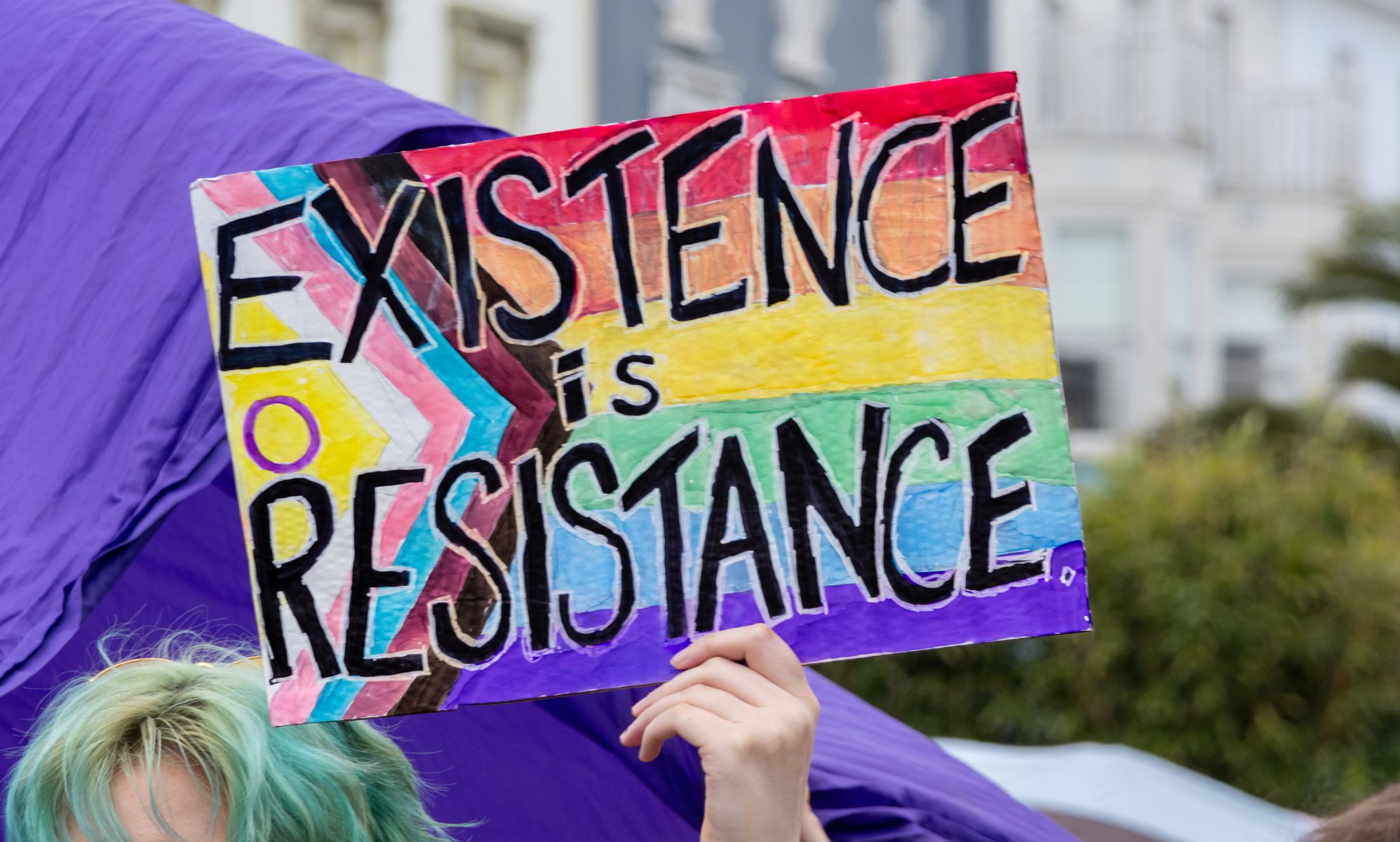 A person holding a sign that reads &quot;existence is resistance.&quot;