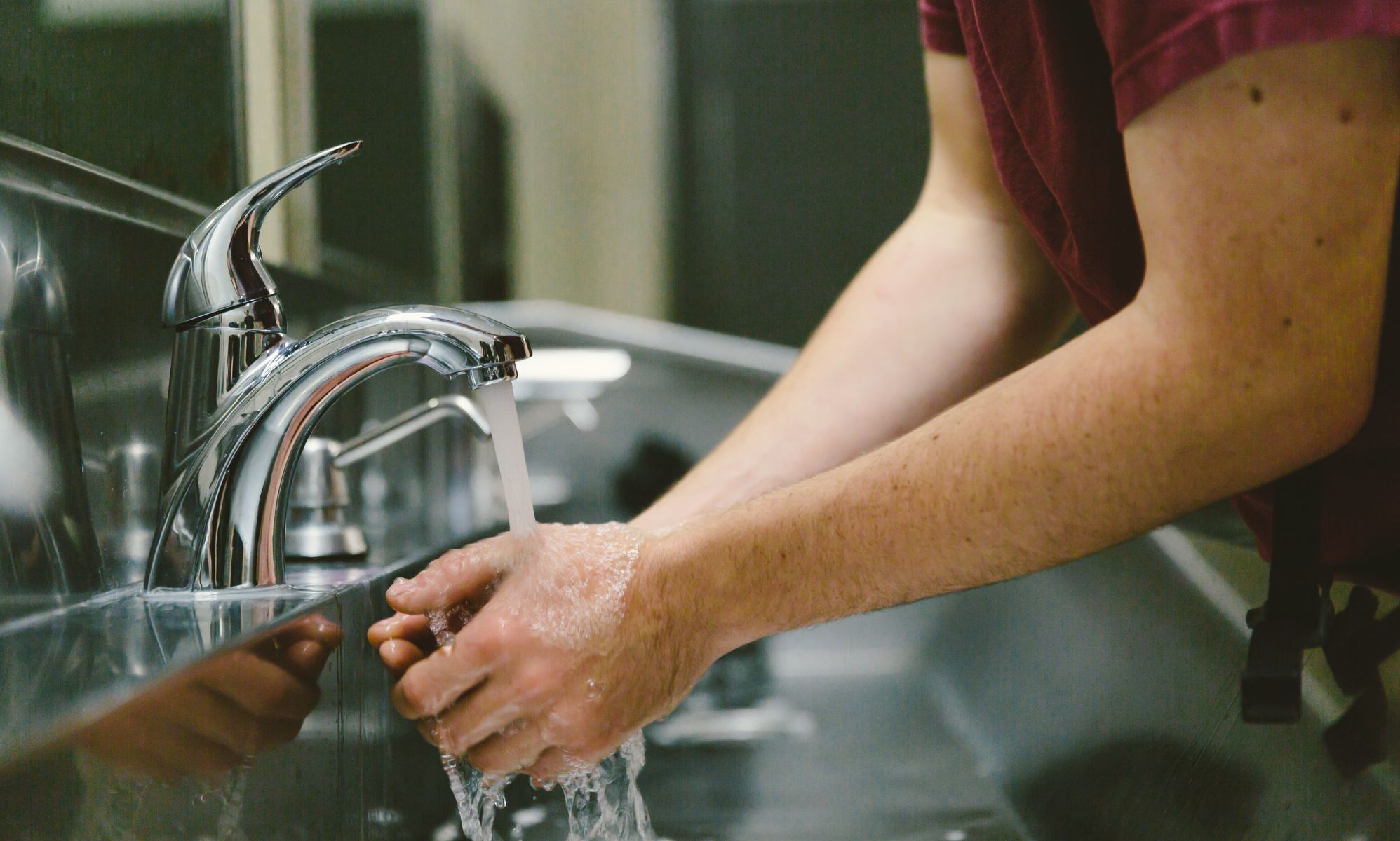 A person washing their hands in a public toilet.