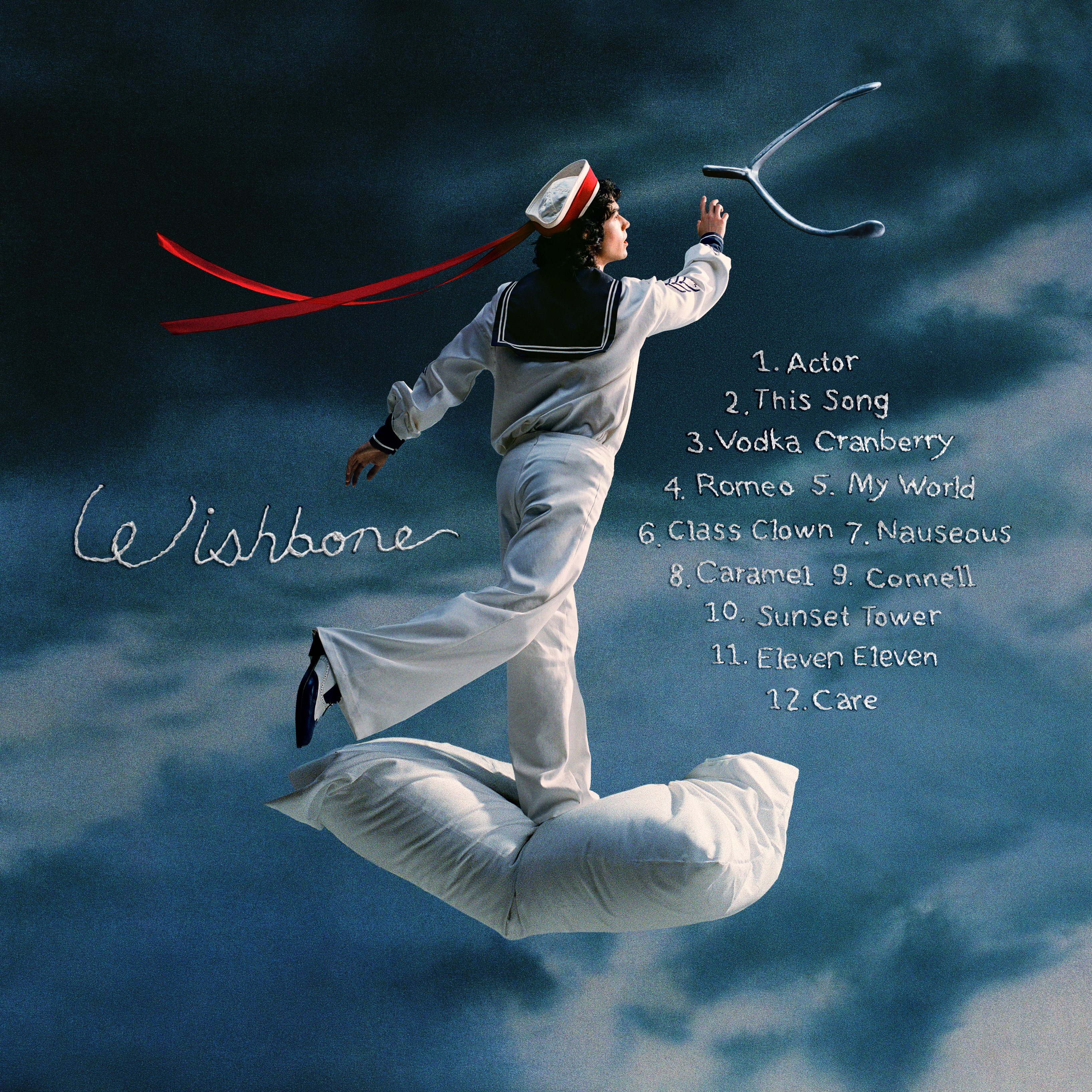 Conan Gray Wishbone album cover, Gray dressed as a sailor, throwing a wishbone while stood on a pillow. Stormy sky behind him with the album track list with a sewn-in look.