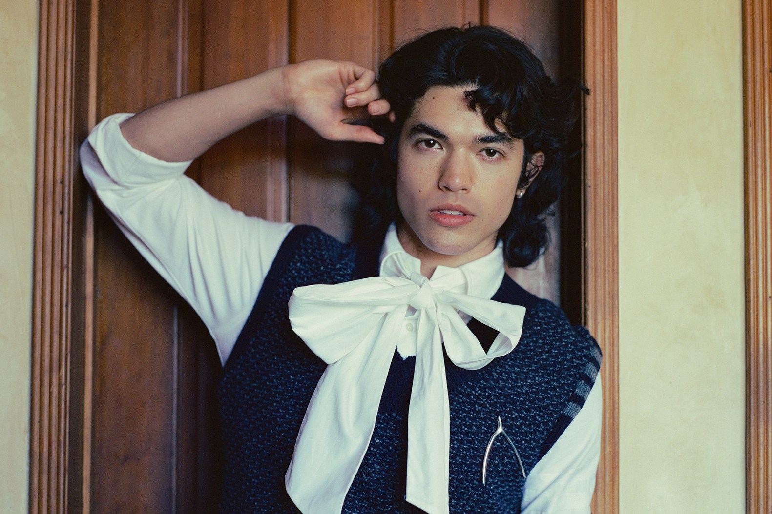 Conan Gray wearing a white shirt with a bow, black vest and wishbone brooch.