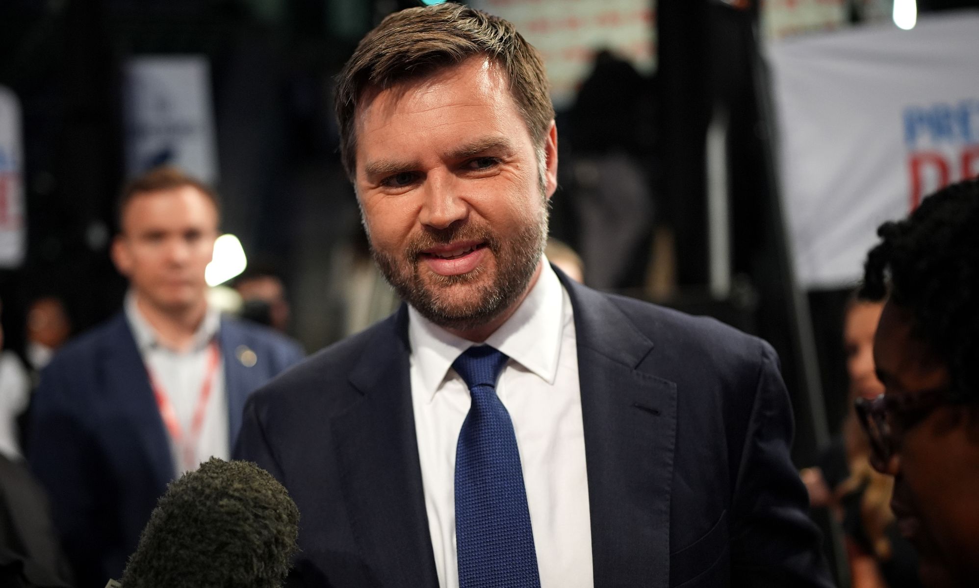 JD Vance smiling as he walks passed a set of reporters.