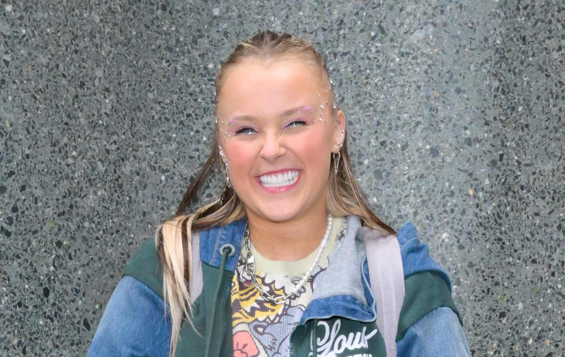 JoJo Siwa in a multi-coloured jacket smiling.