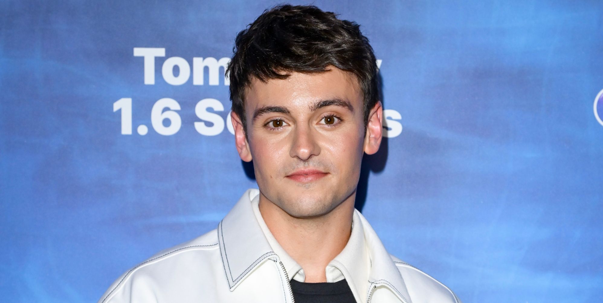Tom Daley in a light jacket smiling as he poses at the premiere of his film 1.6 Seconds.