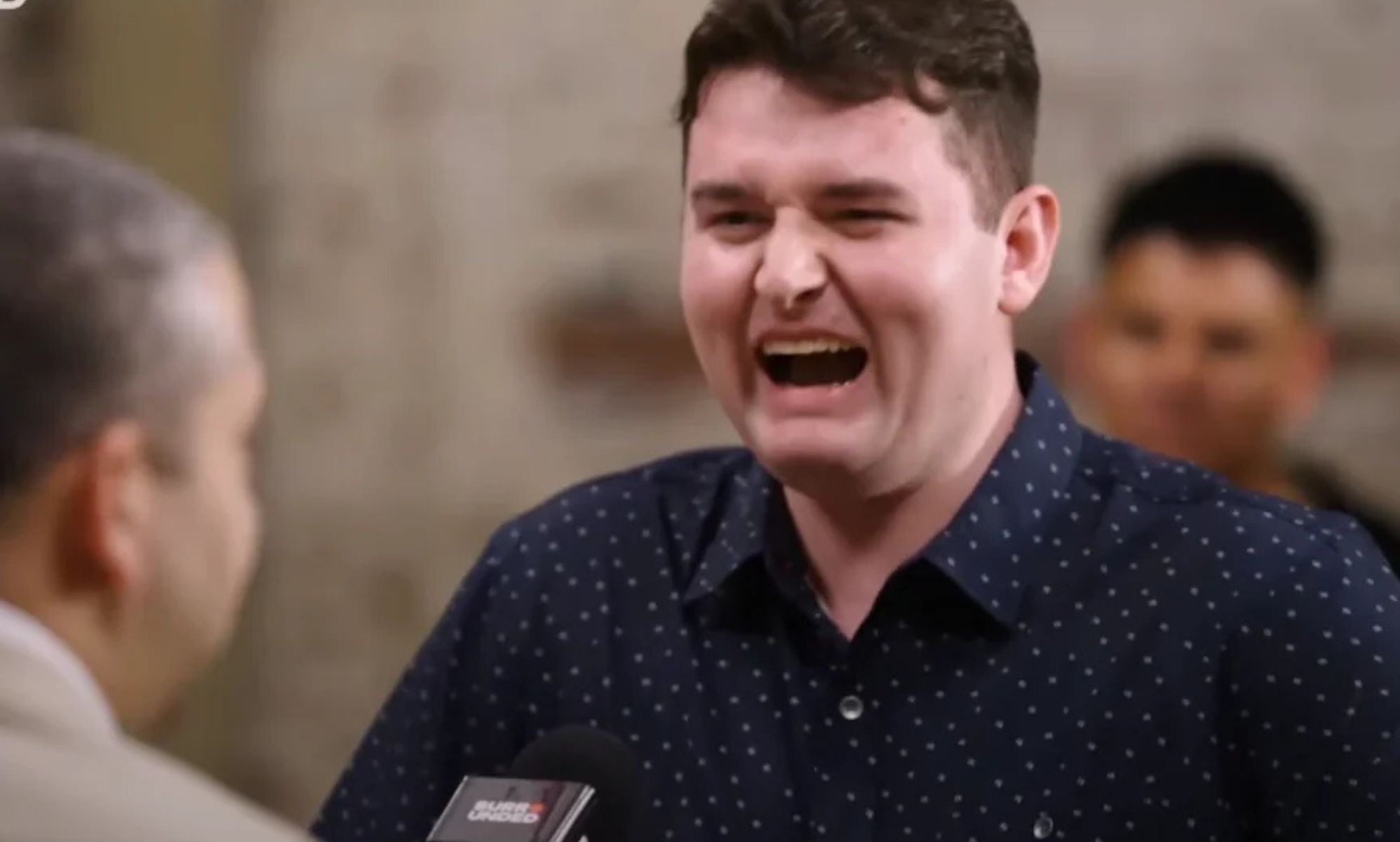 A man with his mouth open looking at another man in a chair.