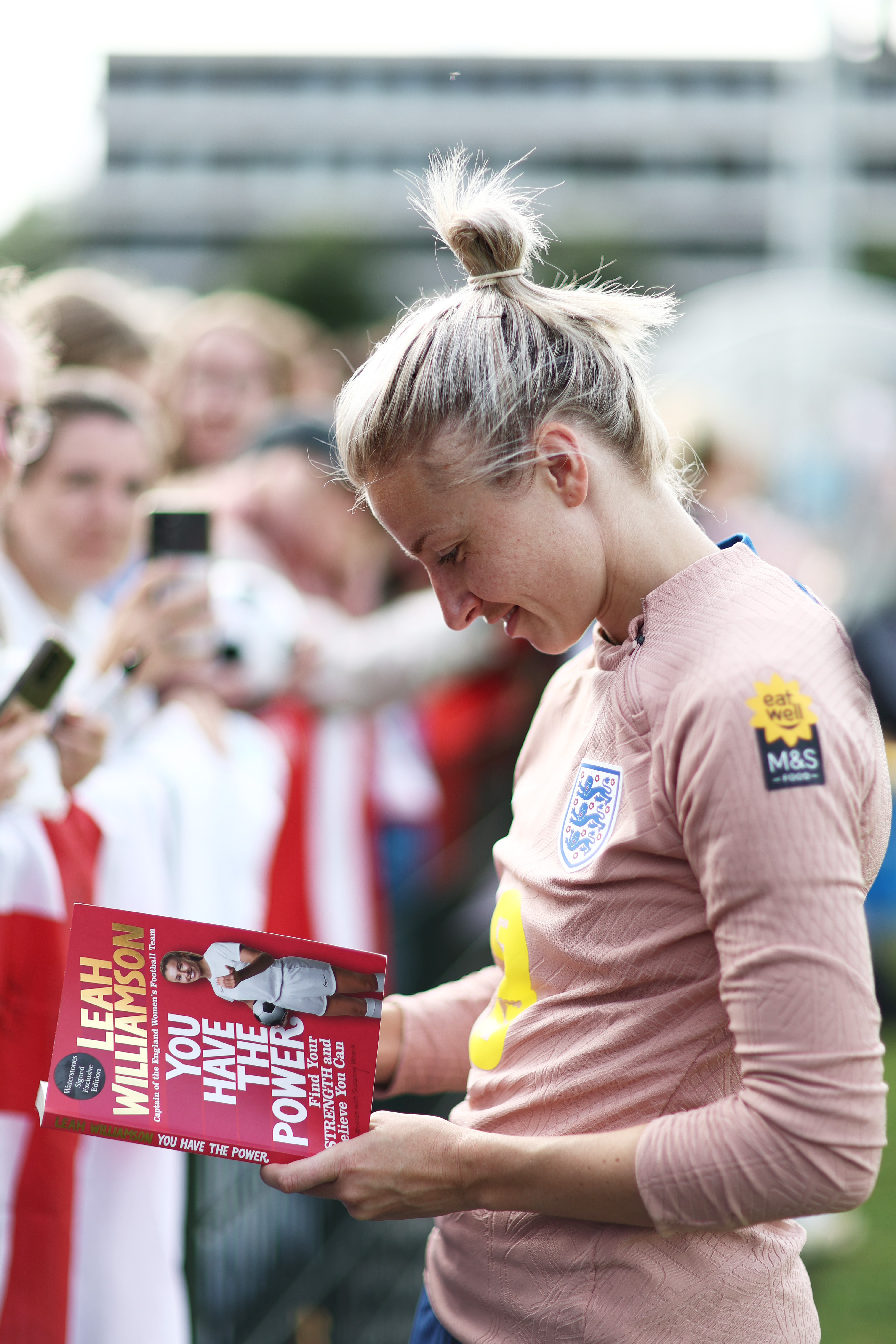 Leah Williamson of England looks at a copy of her book as she greets fans after a Training Session