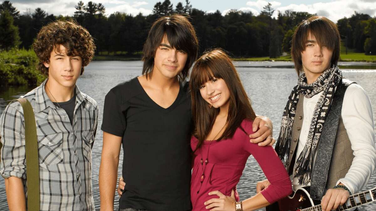 The Jonas Brothers and Demi Lovato posing in front of a lake.